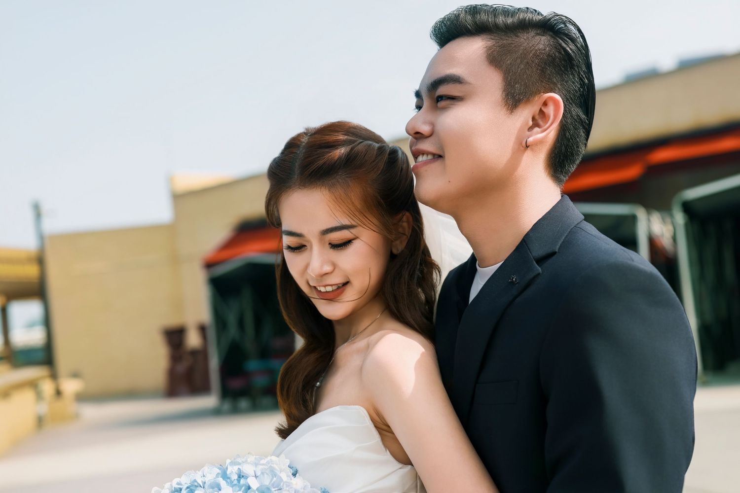 A smiling couple in formal attire sharing a romantic outdoor moment, woman in strapless dress, man in black suit.