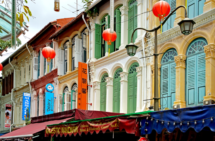 Colorful shophouses with red lanterns in Singapore Chinatown, featuring green shutters and ornate colonial architecture.