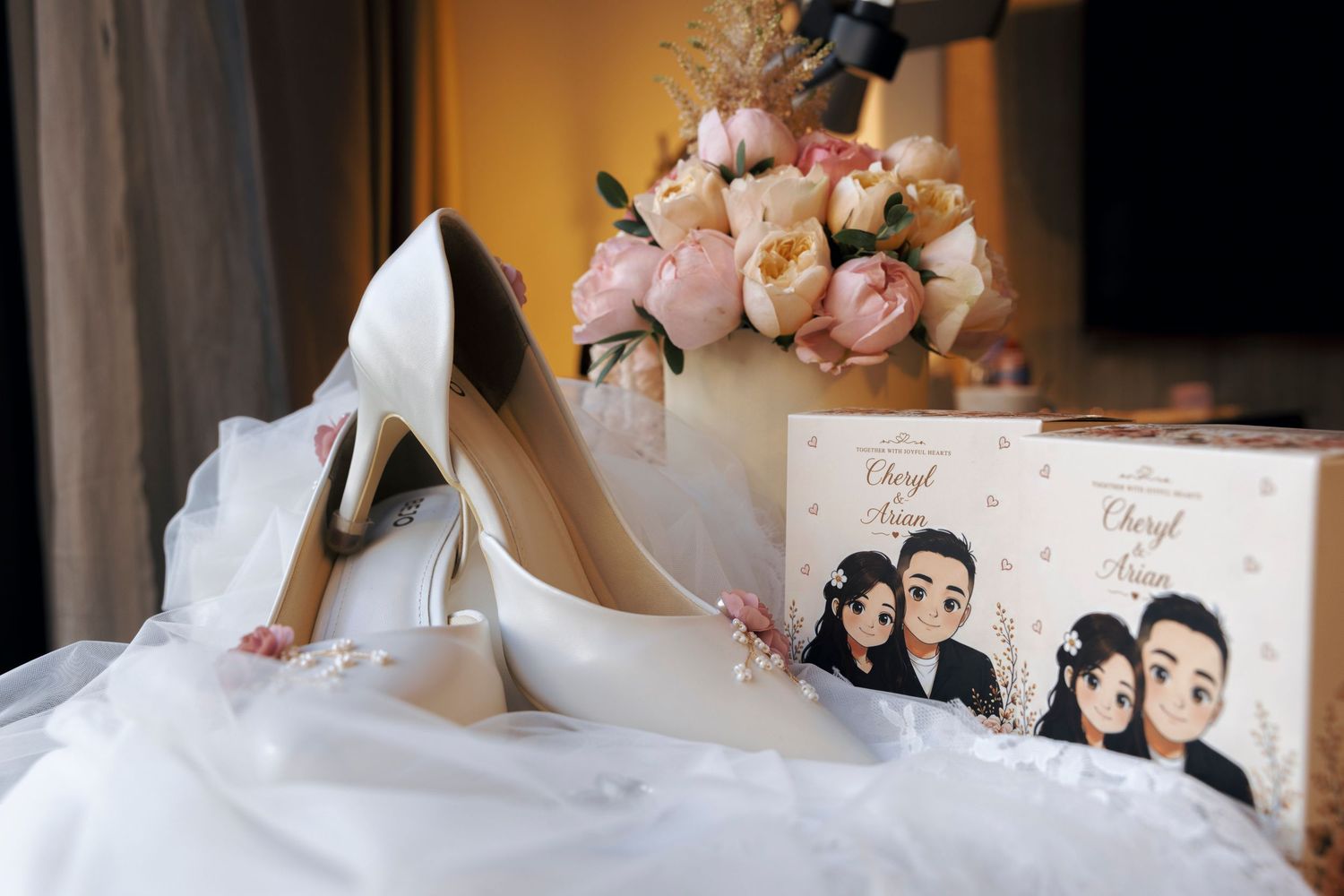 White bridal heels rest beside a floral bouquet and personalized wedding invitation box with couple cartoon illustration.