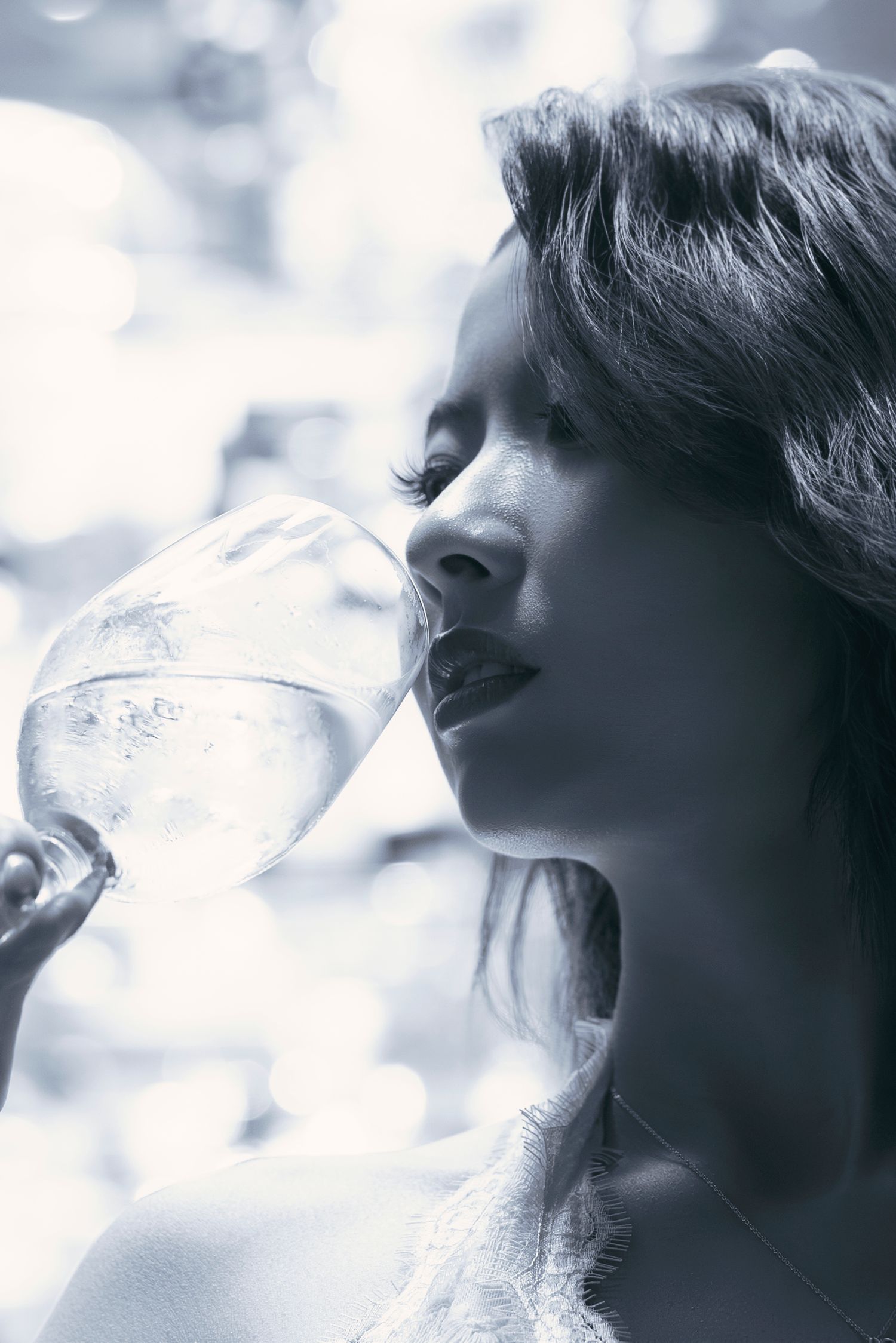 Black and white portrait of a young woman drinking water from a large glass goblet outdoors.