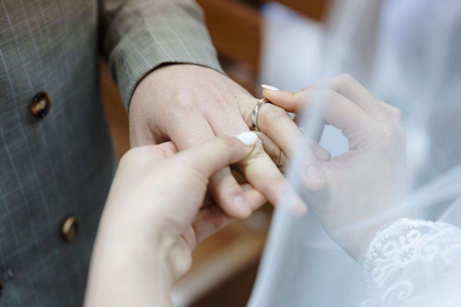 Close-up of a bride placing a wedding ring on the groom's finger during a wedding ceremony.