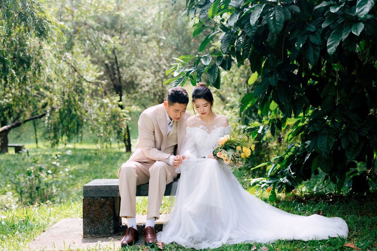 Bride and groom sitting together in a lush garden, reading vows, bride in white gown, groom in beige suit.
