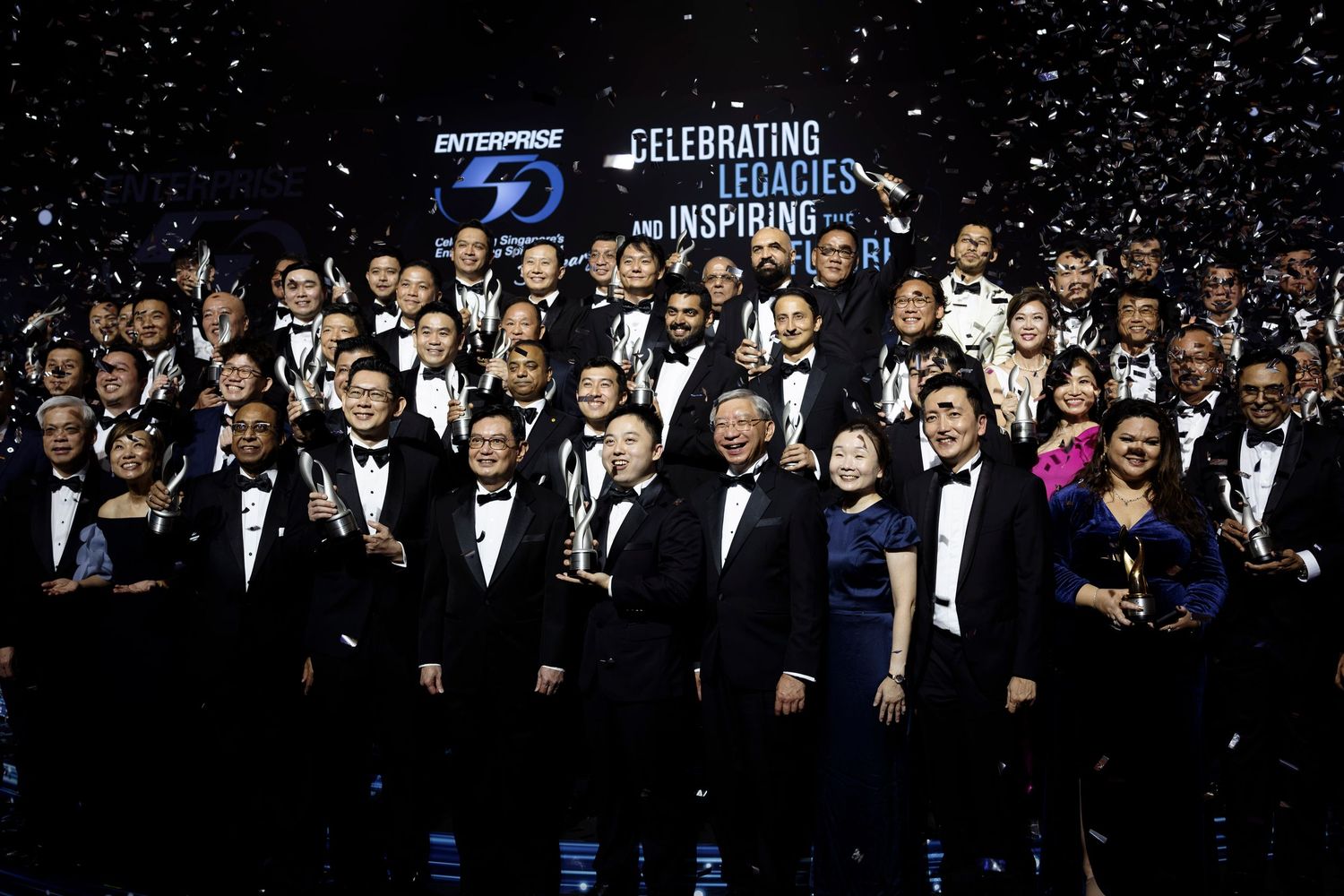 Large group celebrating Enterprise 50 anniversary on stage with confetti under spotlights.