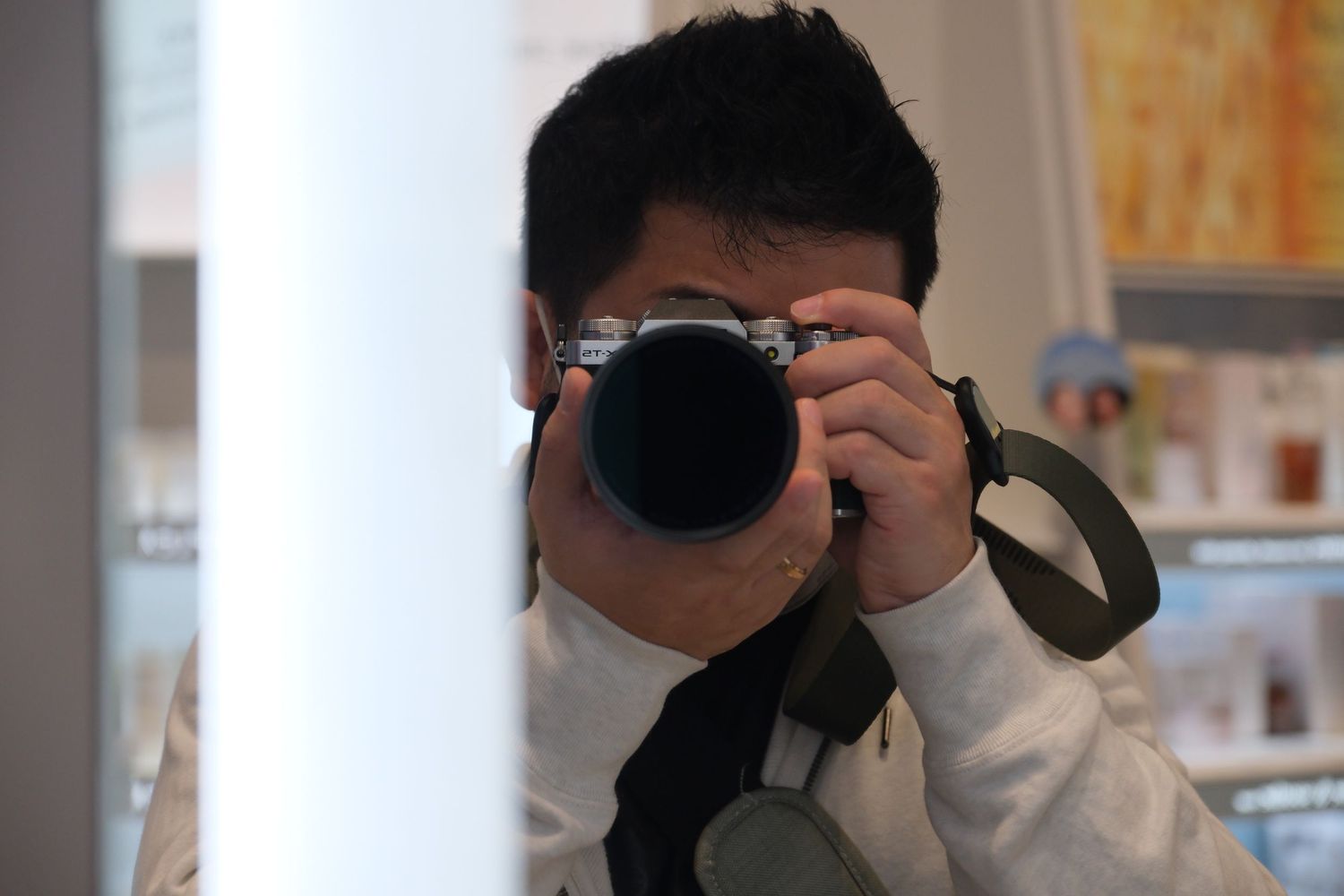 Asian photographer capturing a photo with a DSLR camera, partially hidden behind a wall indoors.