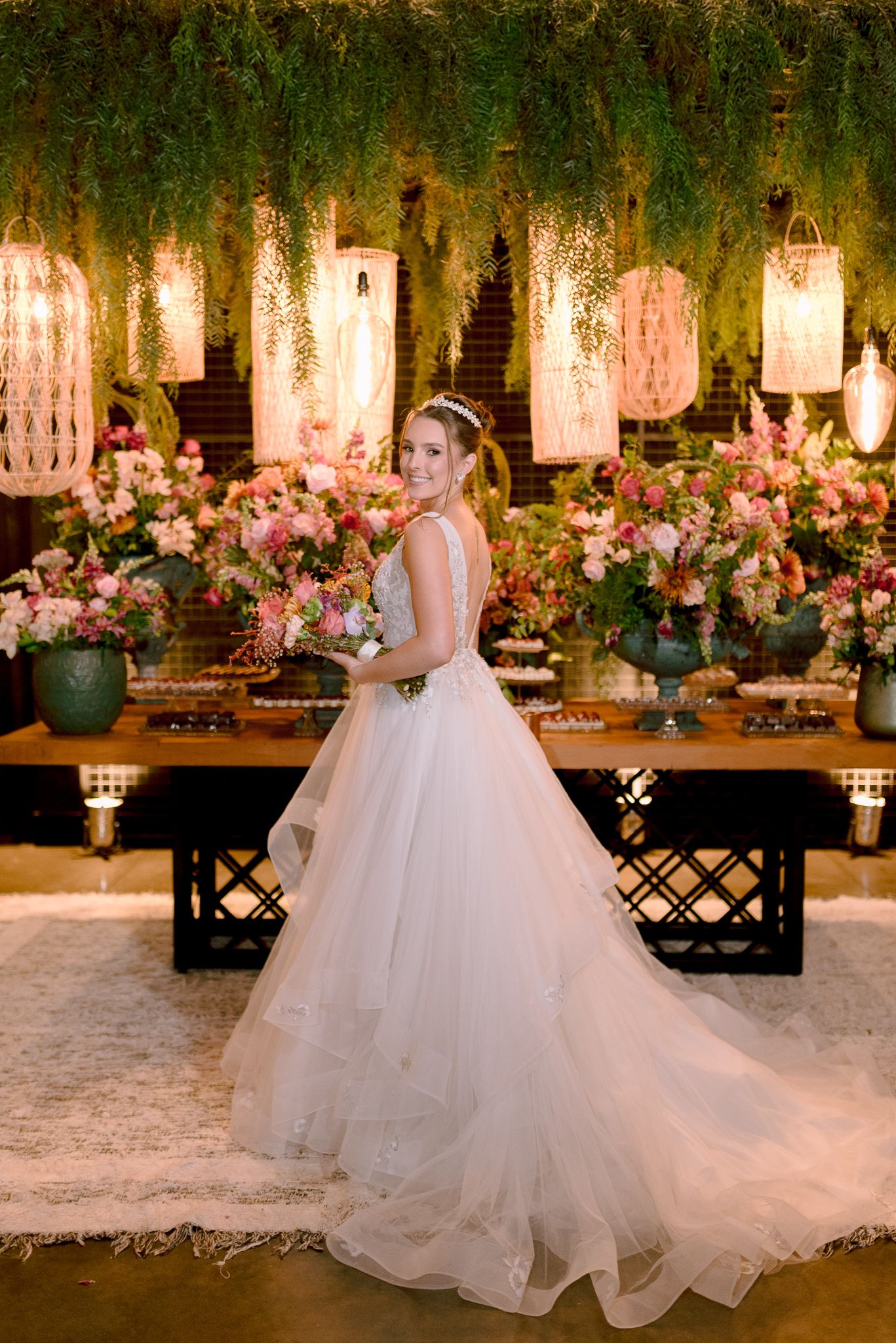 Elegant bride in flowing white ballgown poses in enchanting garden reception setting with twinkling lights and floral decor.