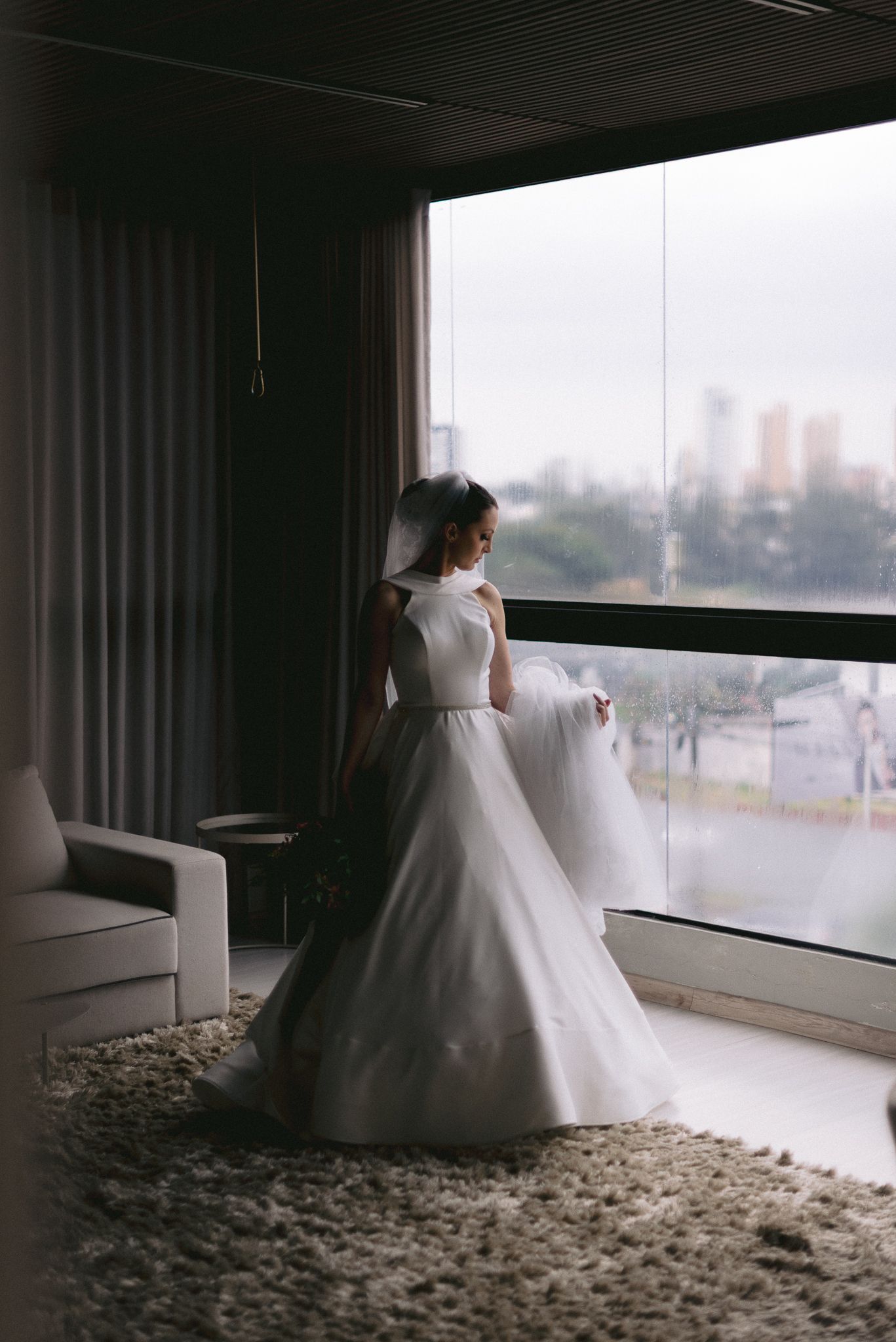 Wedding dress silhouette against floor-to-ceiling windows with city views.