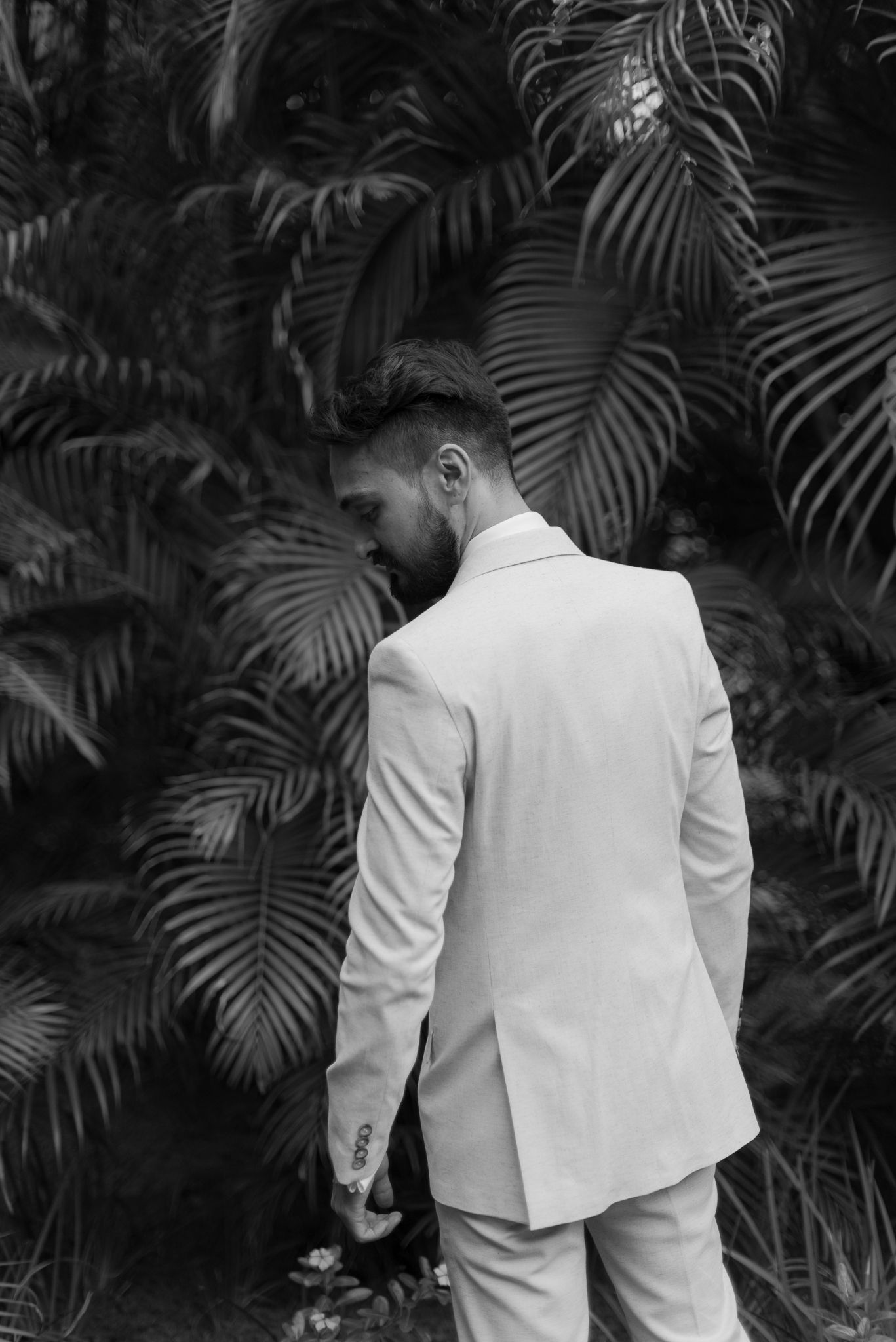 White tuxedo jacket silhouetted against tropical palm fronds in dramatic black and white.