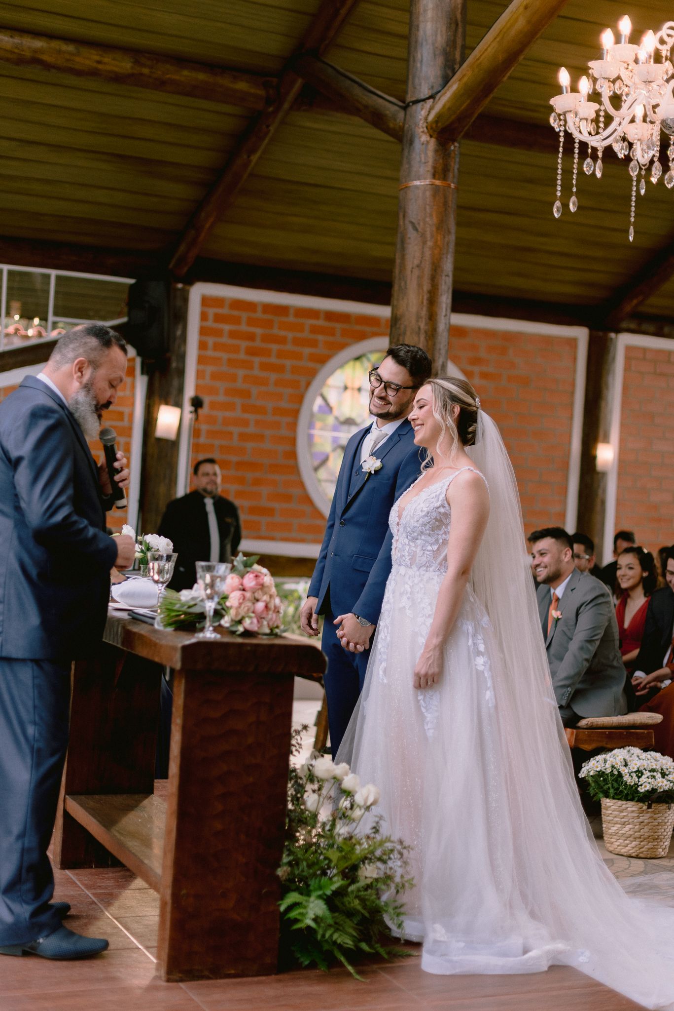 Wedding ceremony in a rustic venue with exposed beams and chandelier.