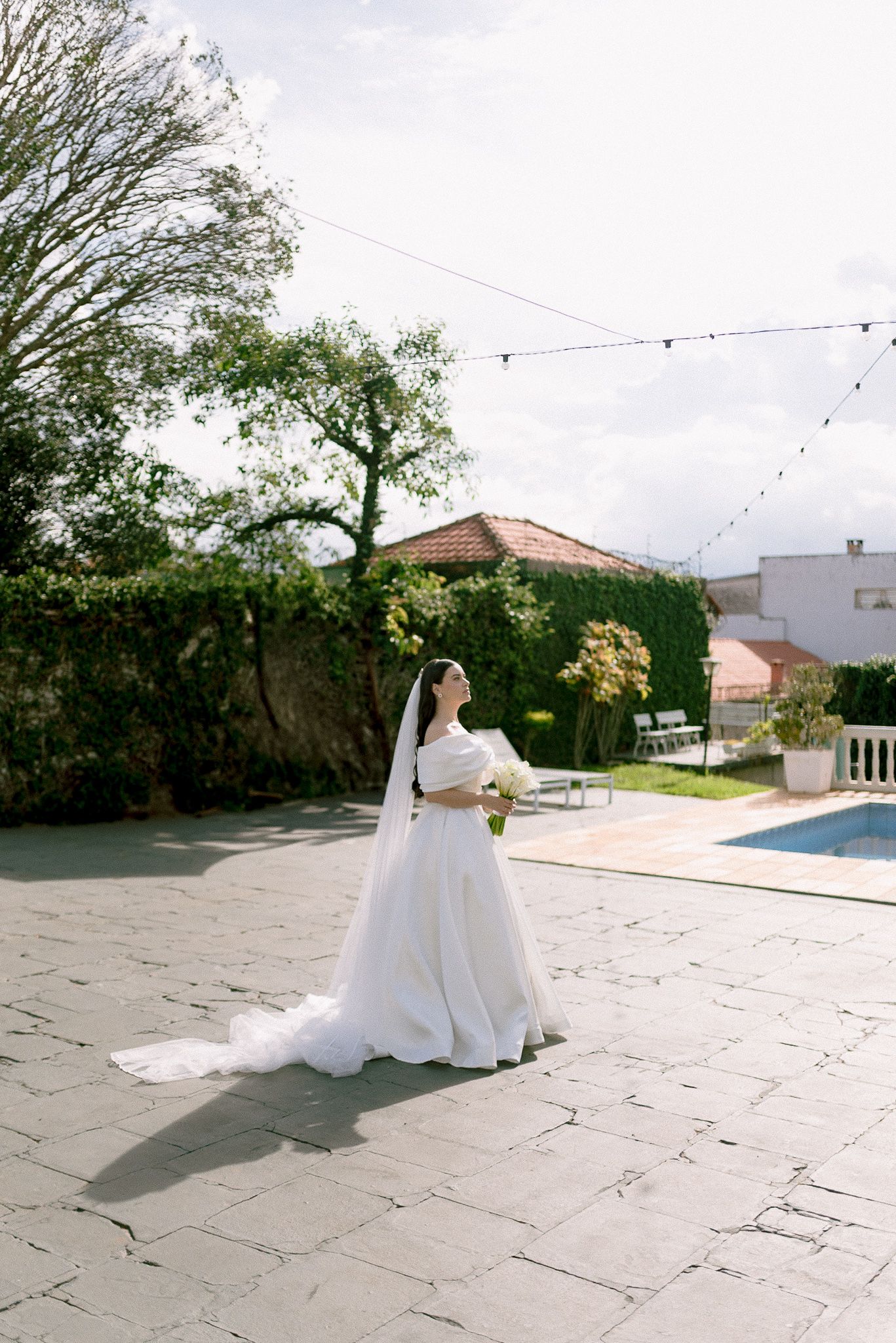 A flowing white wedding gown spreads across a stone patio with garden string lights overhead.