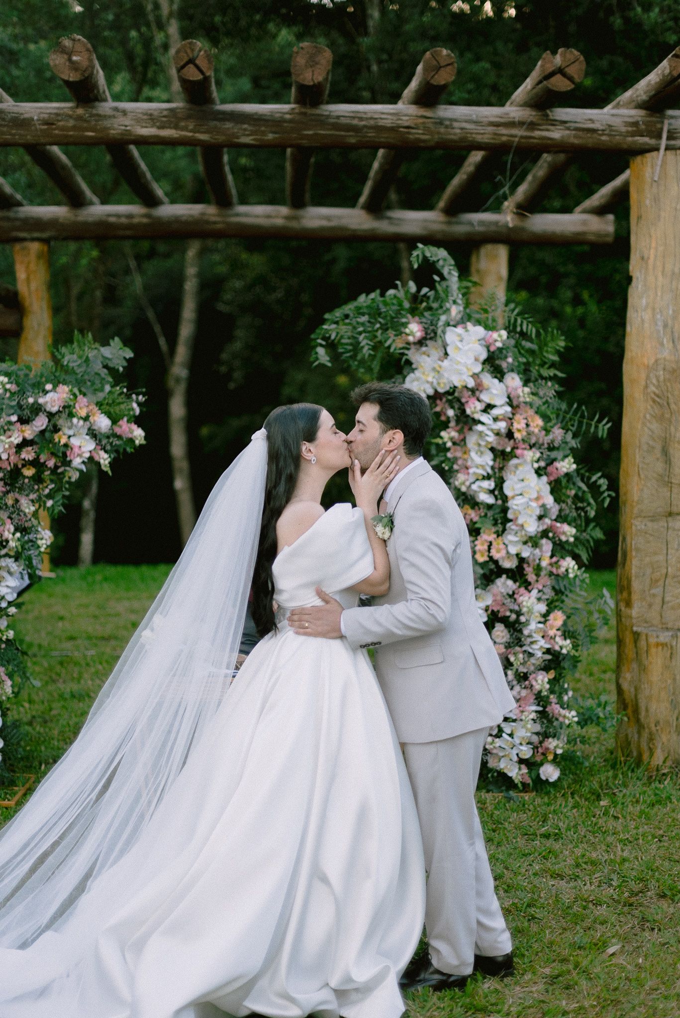 A romantic outdoor photo sequence shows newlyweds sharing kisses under a rustic wooden pergola decorated with pink flowers.
