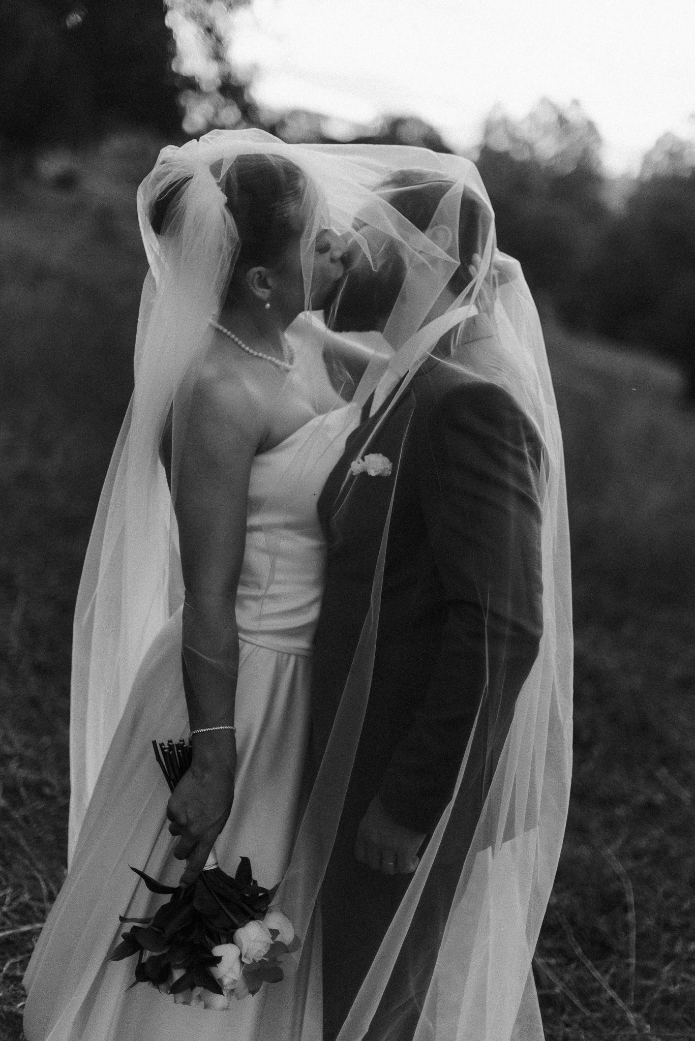 A romantic black and white wedding photo series showing couples embracing under flowing white veils in an outdoor setting.