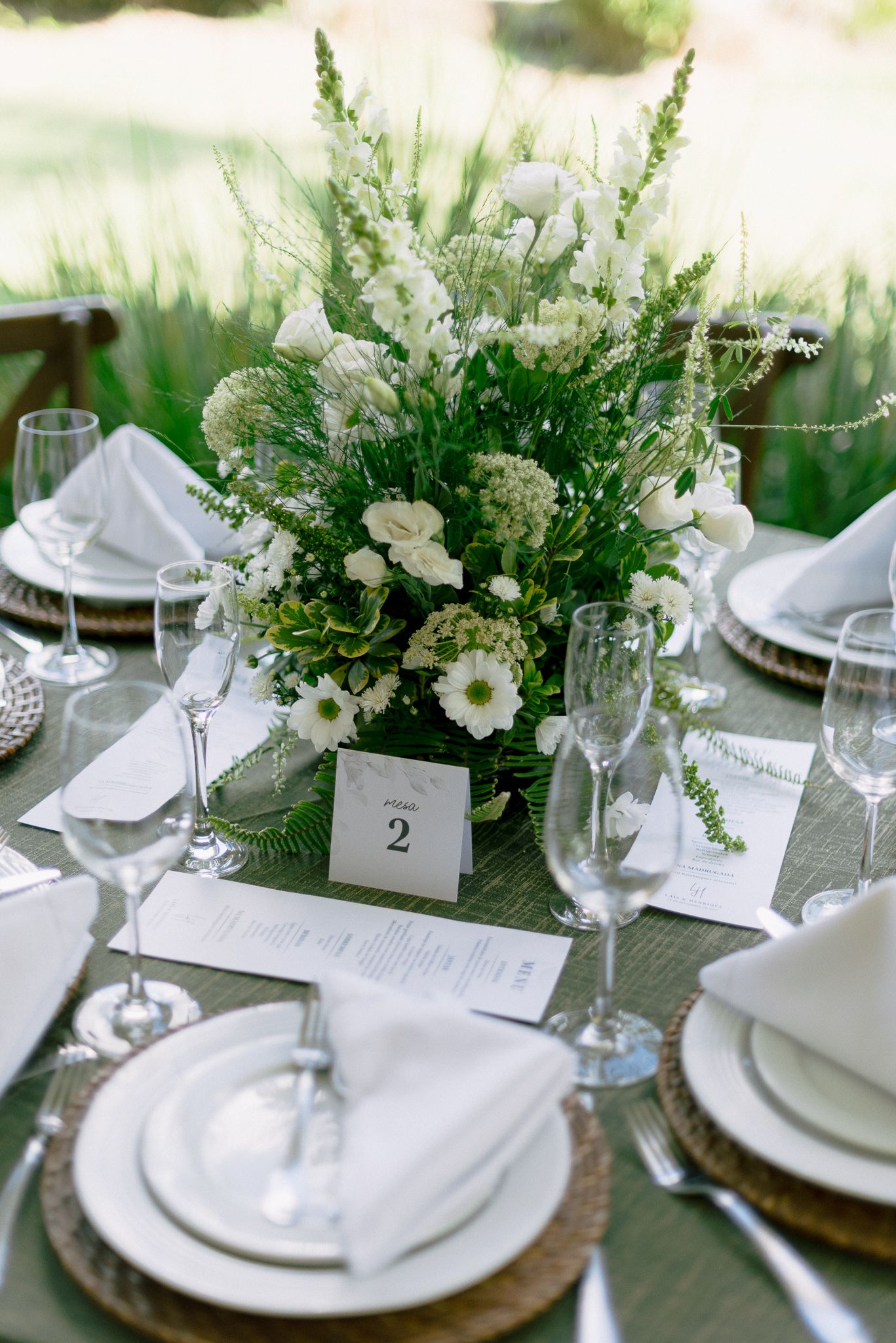 Elegant table setting with white plates, greenery centerpieces, and table numbers for a formal dining event.
