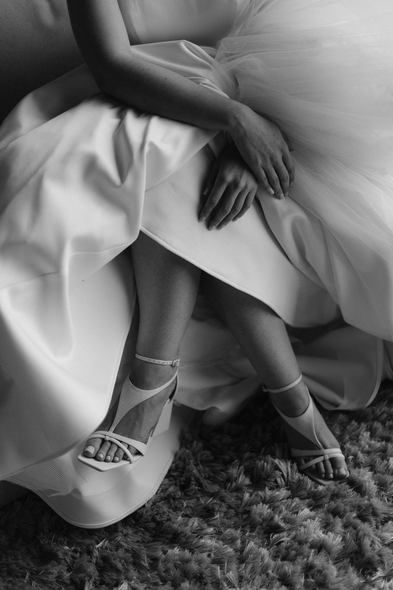 Close-up details of white bridal shoes and dress hem against a gray carpet.