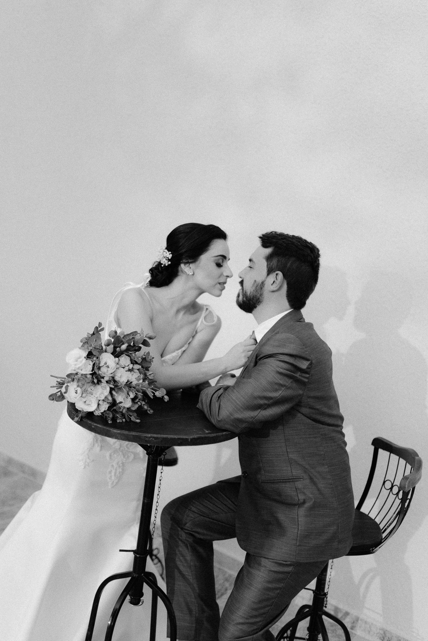 An artistic black and white photo of newlyweds posed on vintage bar stools.