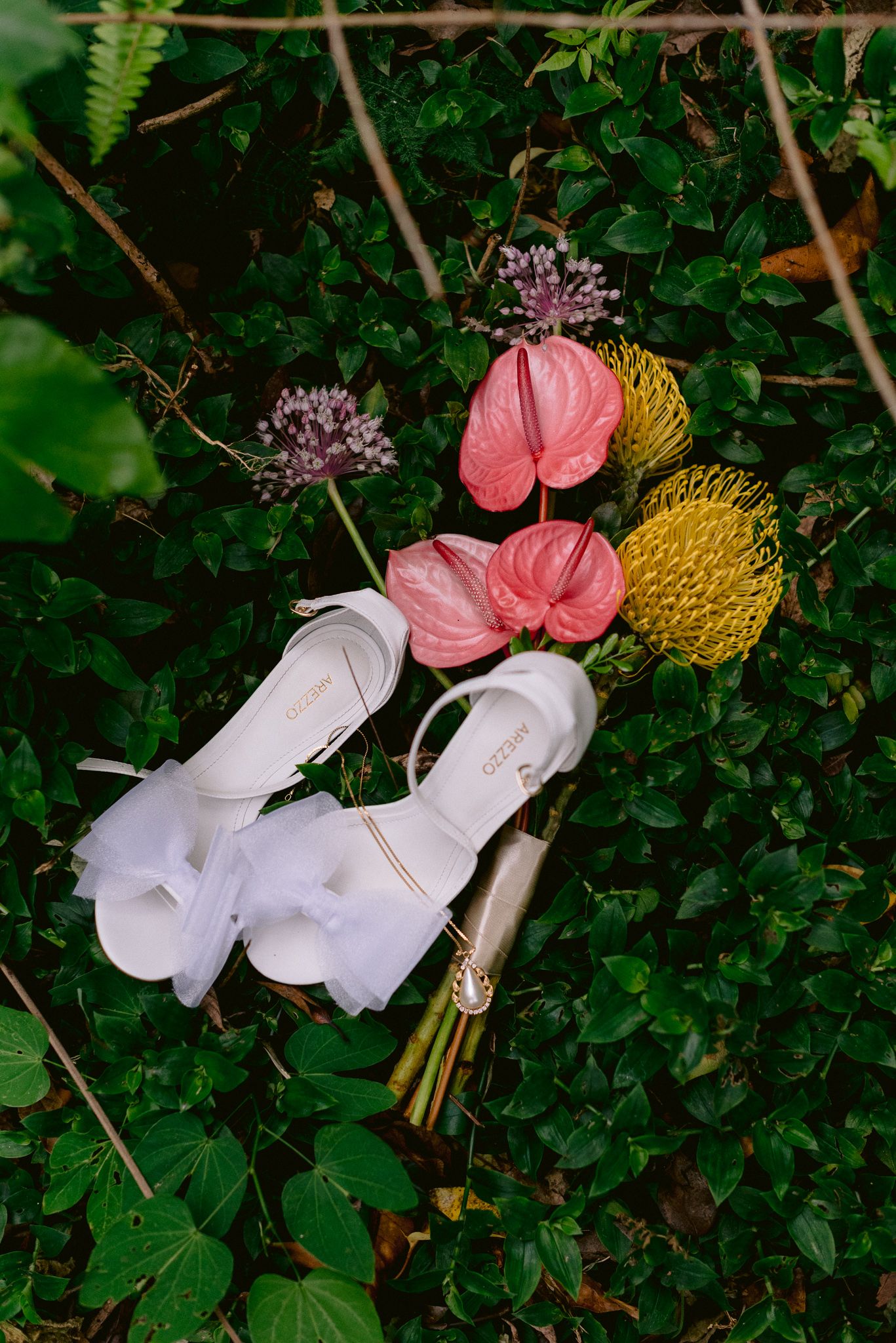 White bridal shoes and coral bouquet arranged on green foliage.