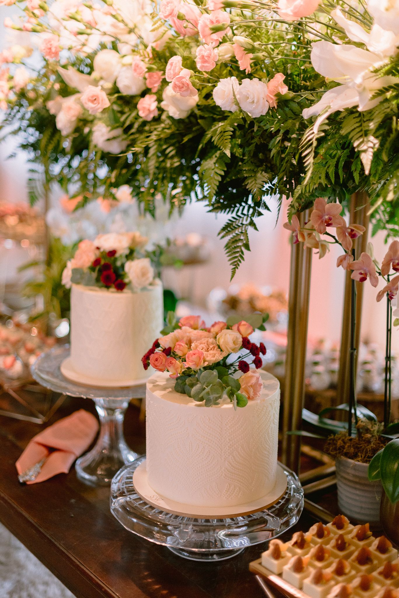 Wedding dessert display featuring elegant white cakes adorned with pink flowers and greenery.