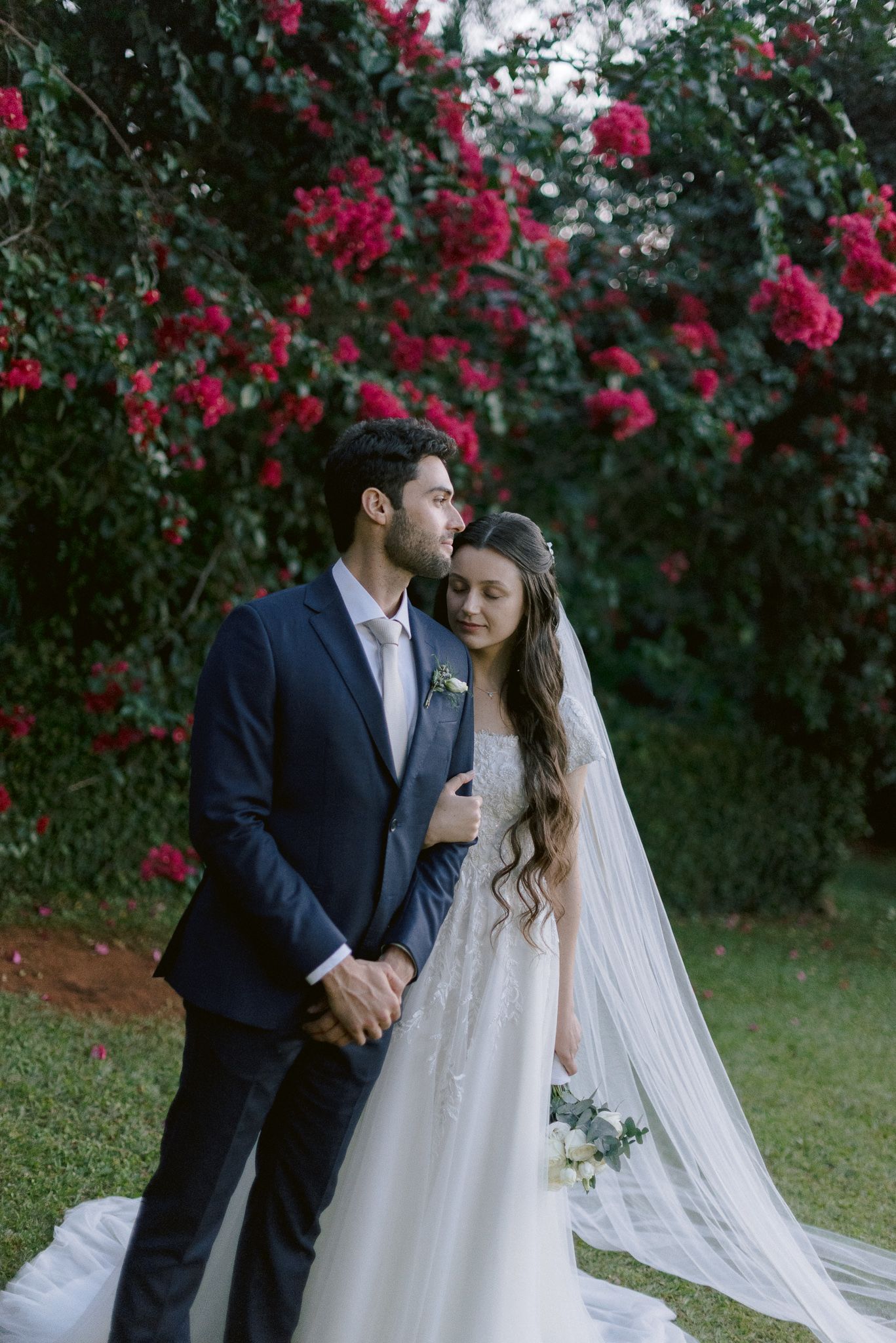 Couple shares intimate moments in lush garden setting with vibrant pink flowers and flowing white bridal veil.
