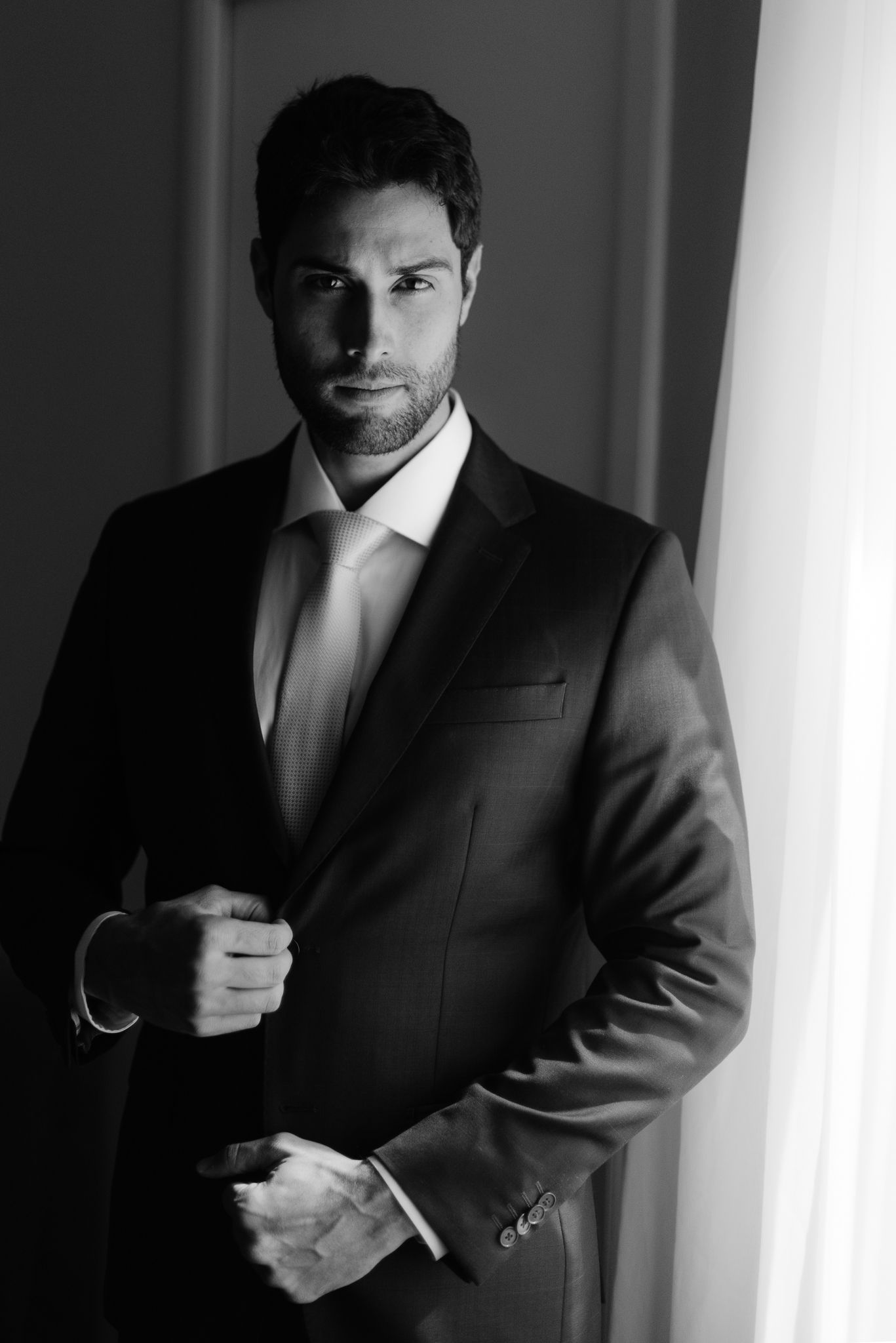 A moody black and white series of shots showing a man in a dark suit adjusting his clothing in dramatic lighting.