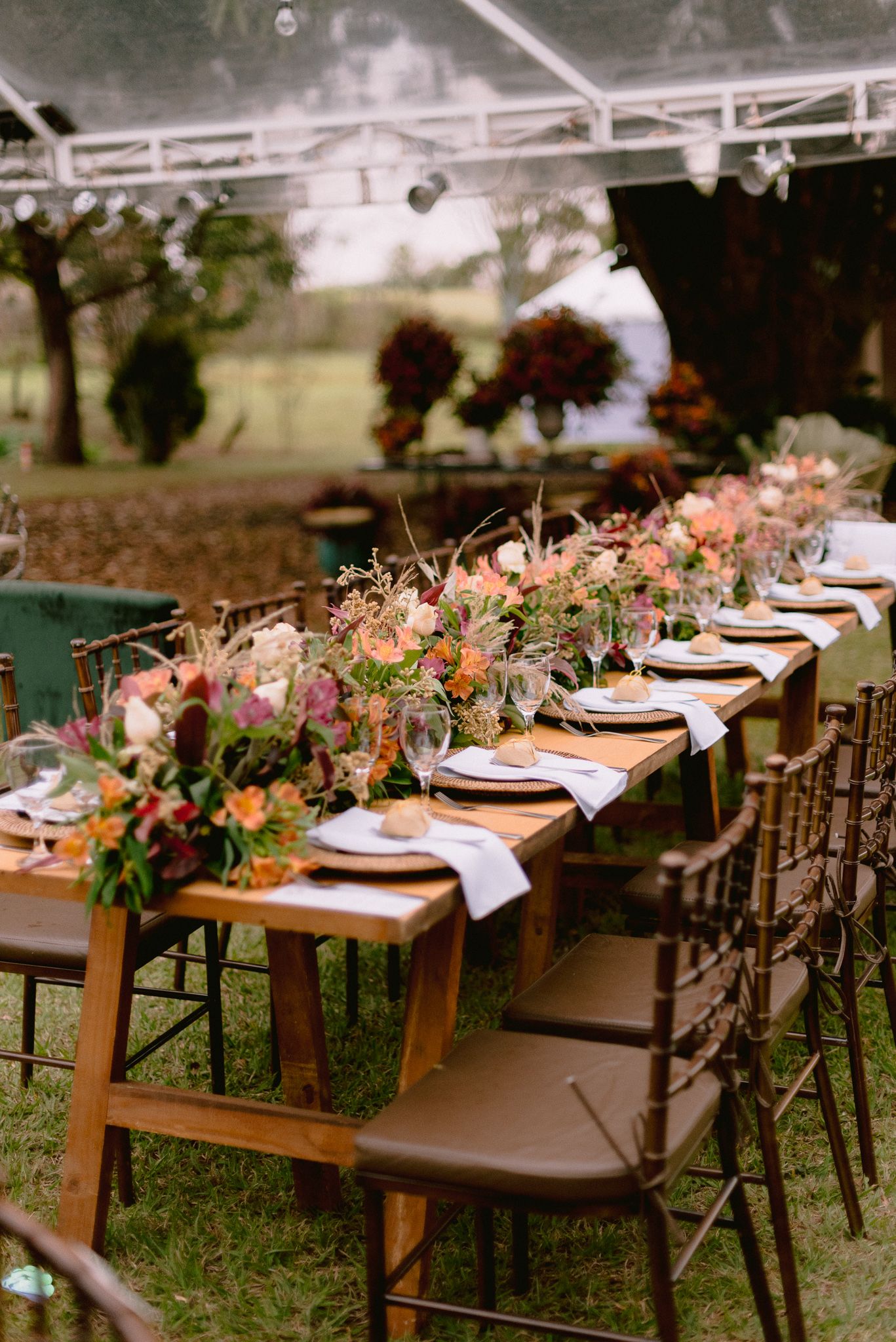 Rustic outdoor wedding reception table with wooden chairs and floral arrangements.