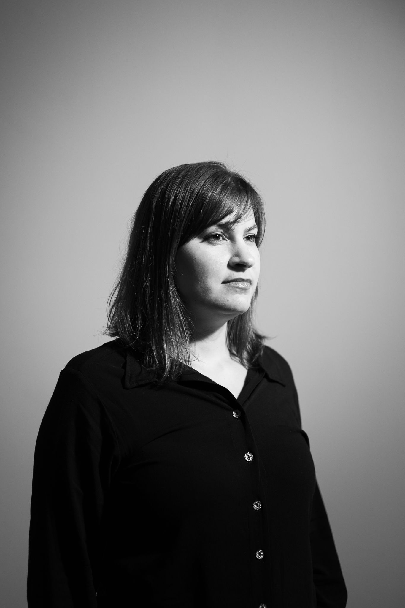 Black and white portrait of a woman with bangs wearing a dark button-up shirt against a neutral background.