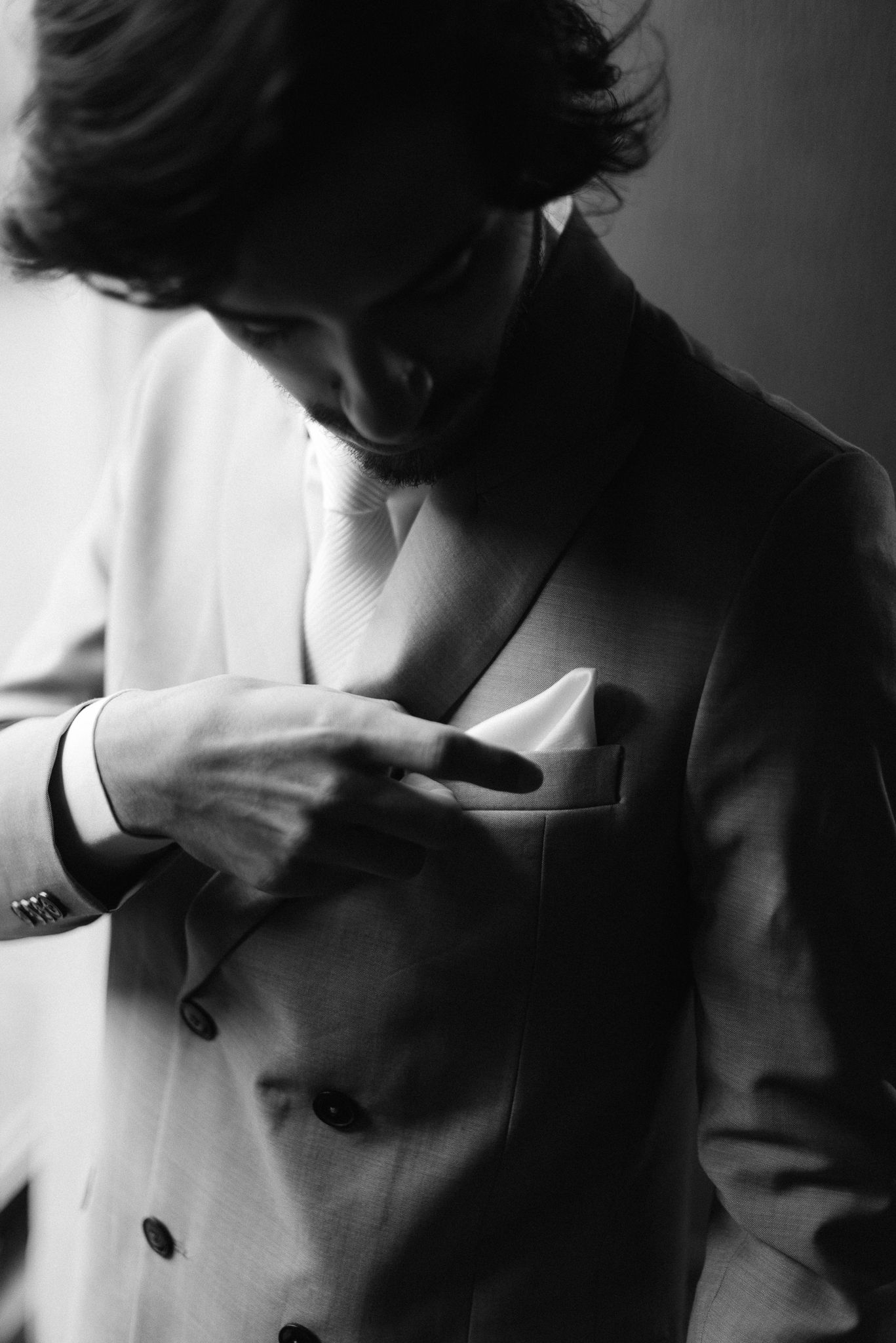 Black and white photo of someone in a white suit jacket reaching into the breast pocket, shot in dramatic lighting.