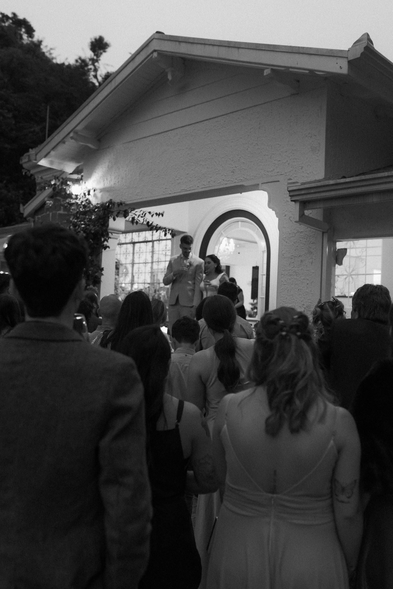 Wedding guests gathering outside a white building at dusk.