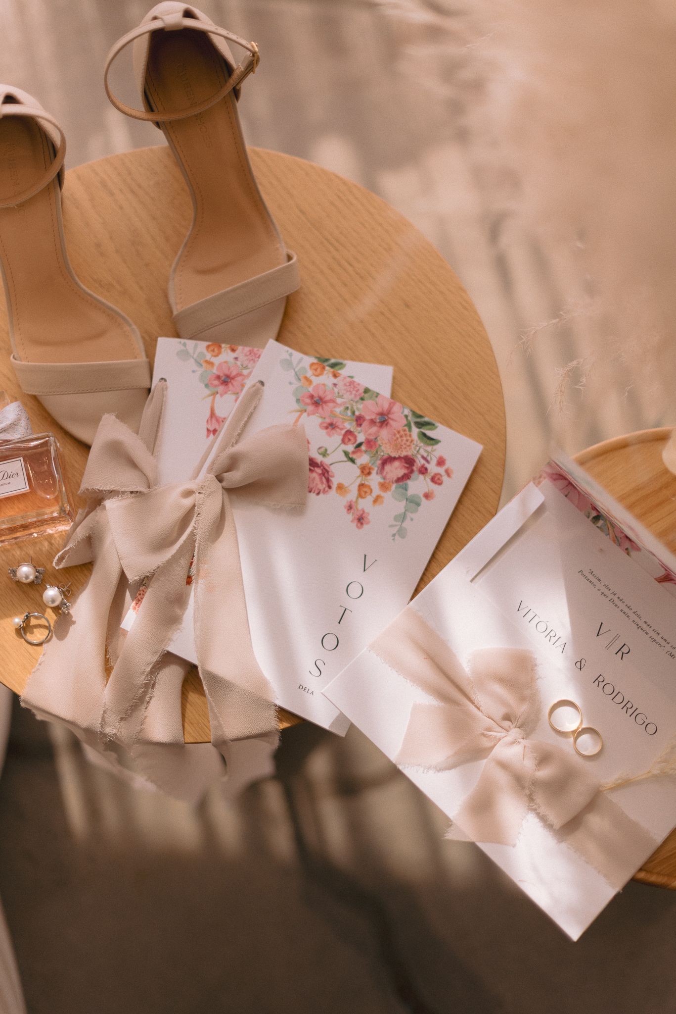 Wedding rings and cards with delicate floral designs lay scattered on a beige surface in soft lighting.