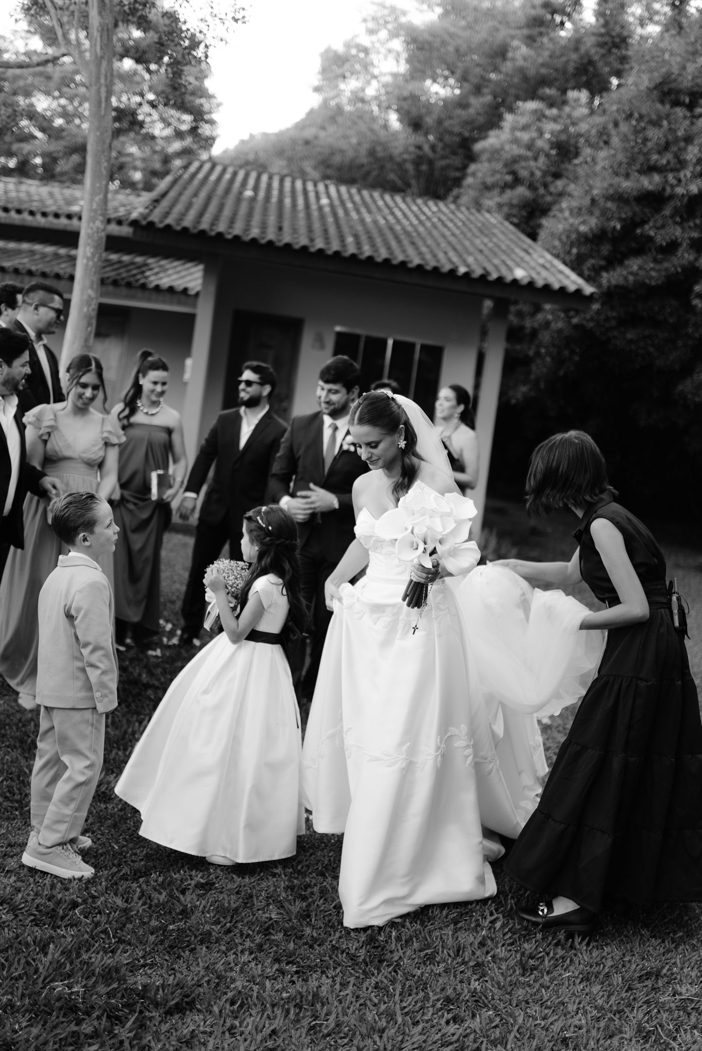 Black and white photo of wedding party dancing in a line outdoors near Spanish-style buildings.