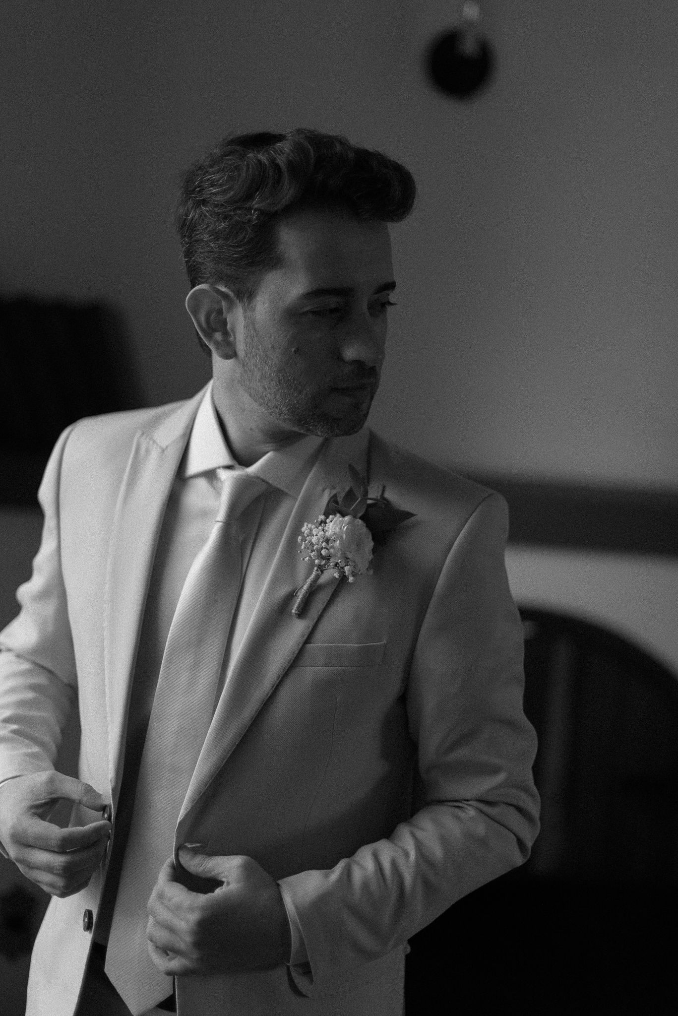 Black and white closeup detail shots of a groom wearing a white tuxedo jacket with boutonniere during wedding prep.