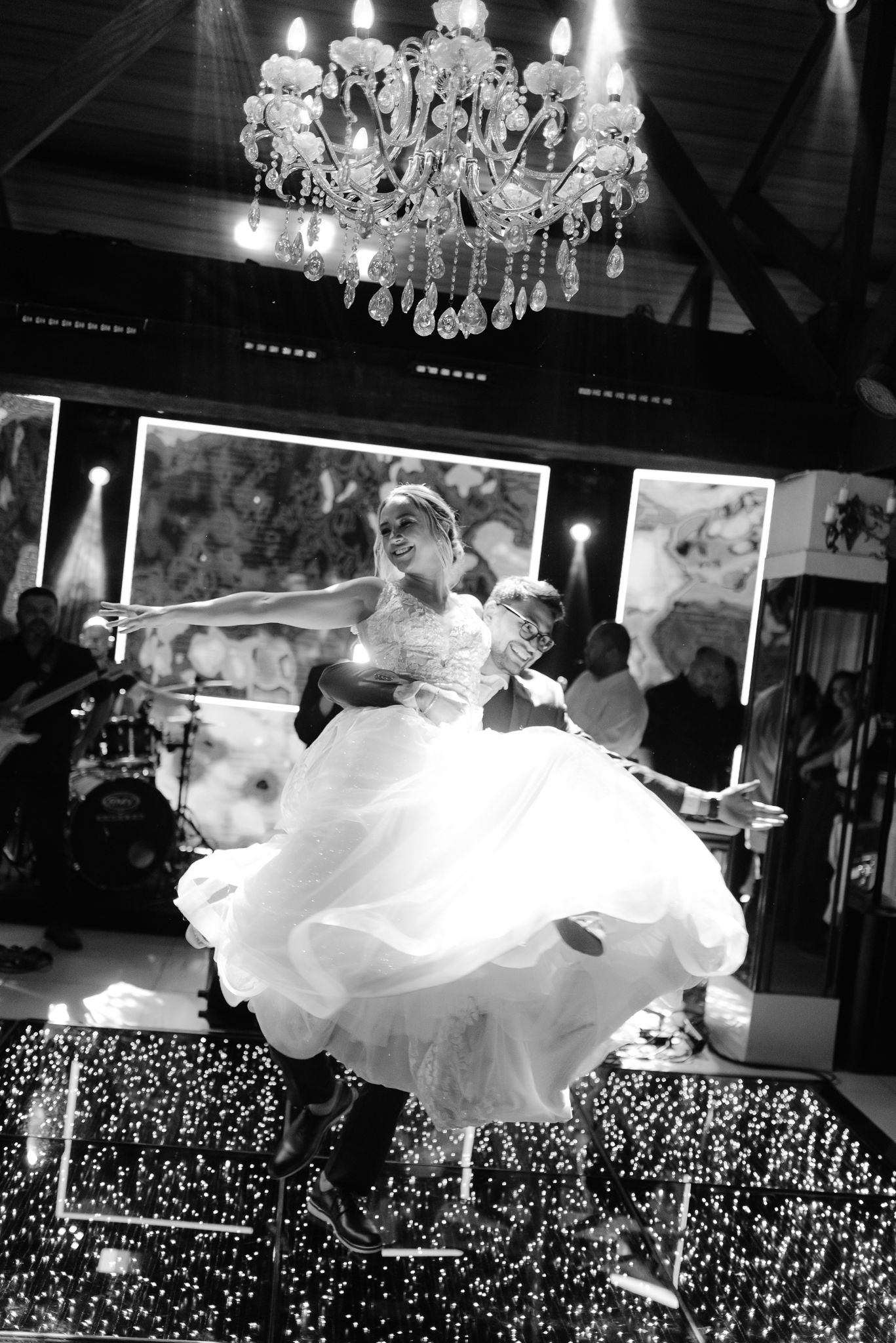 Bride's dress flows dramatically during a dance spin on a sparkling light-covered dance floor.