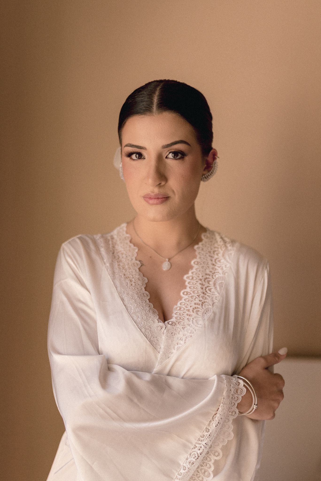 Portrait of bride in white lace robe against warm neutral background.
