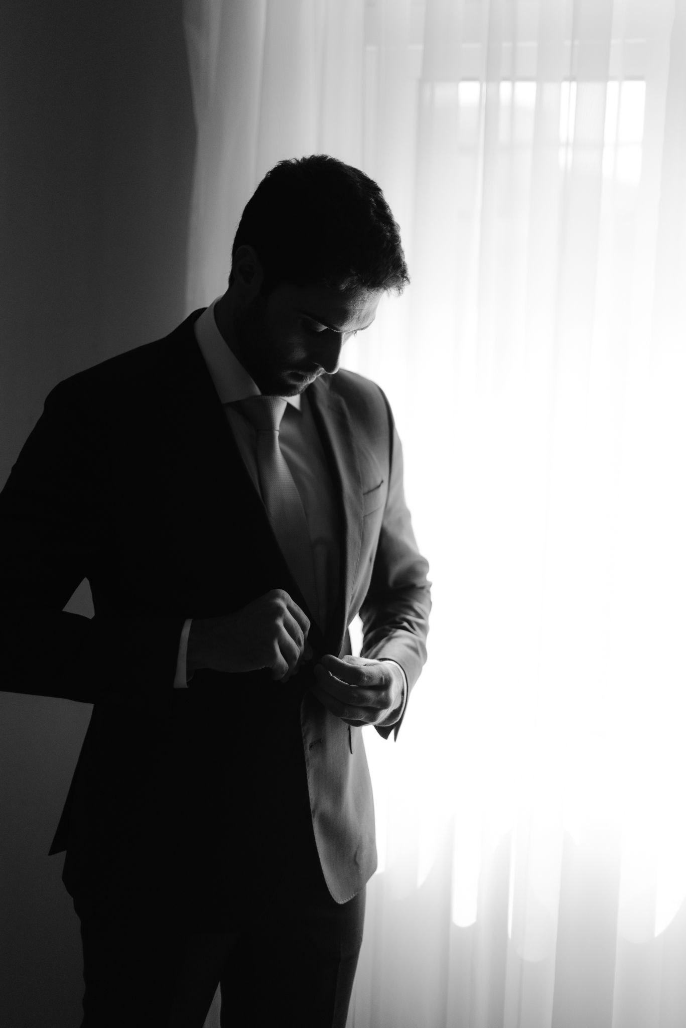 Silhouetted man in black suit coughing into elbow shown in multiple frames against white window light background.