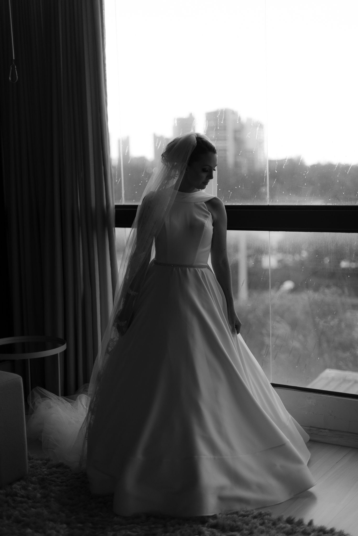 Dramatic silhouette of wedding dress against window with city view.
