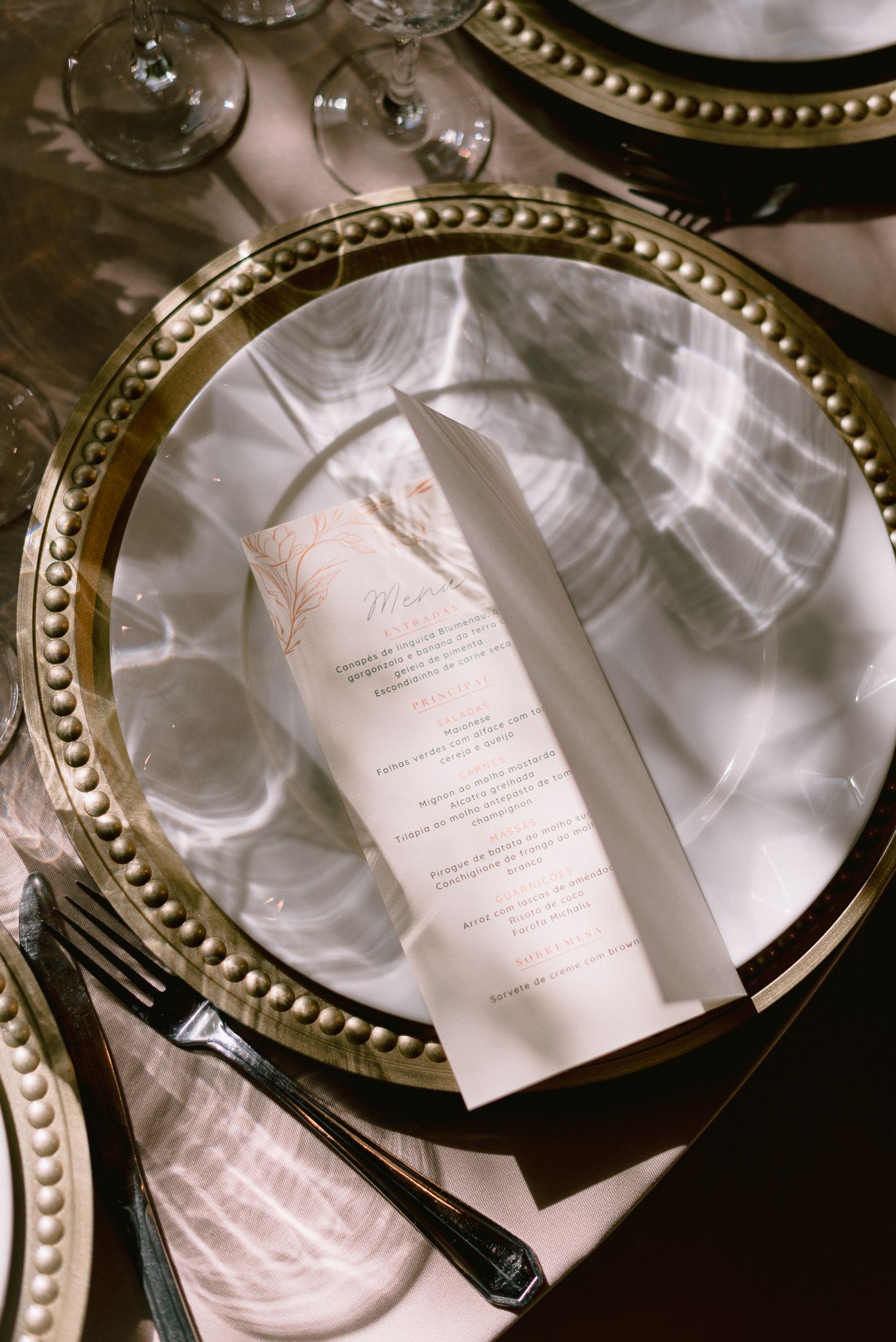 Wedding menu cards placed on gold-rimmed charger plates with elegant place settings.