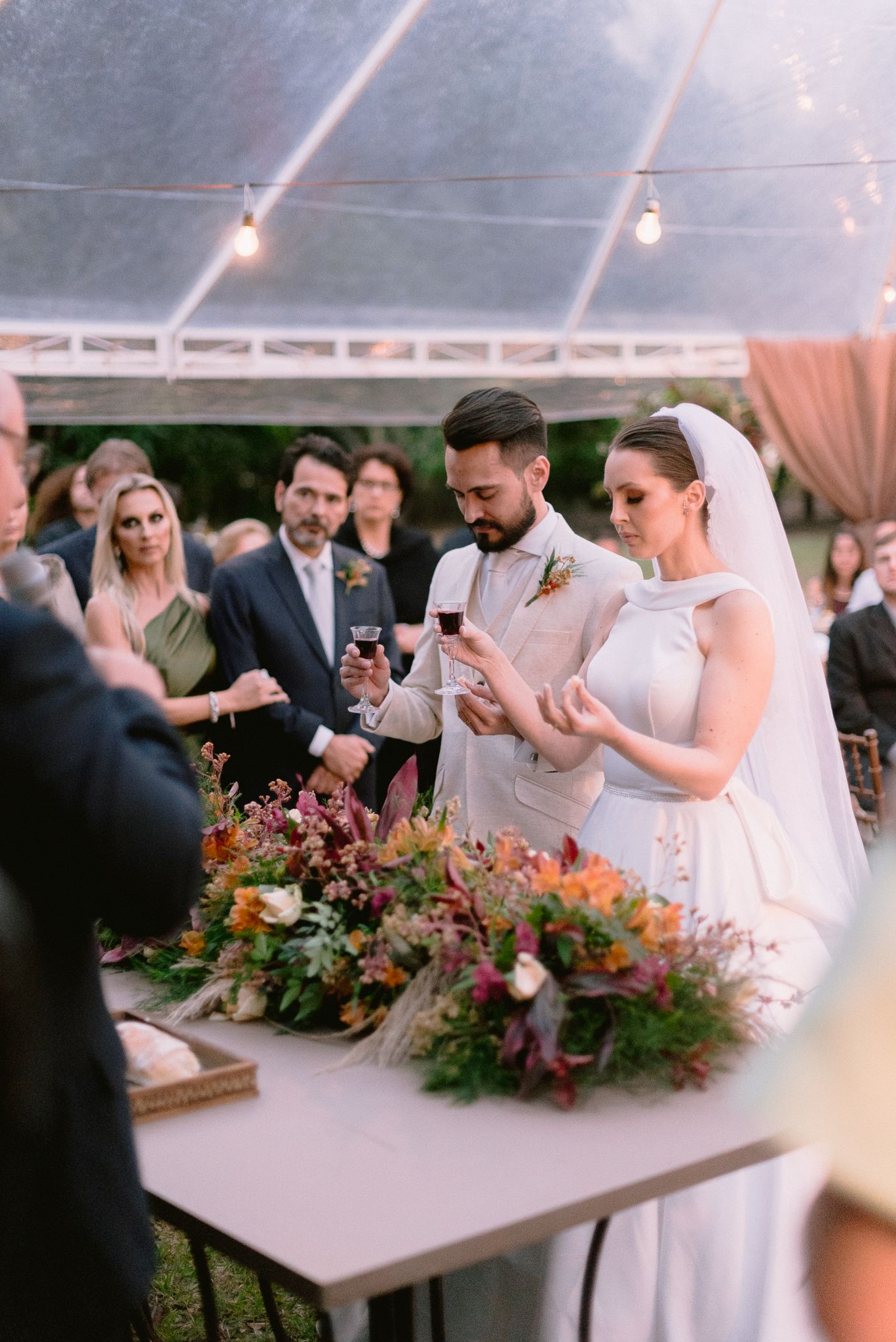 Reception guests gathered around a long table with beautiful floral arrangements under string lights.