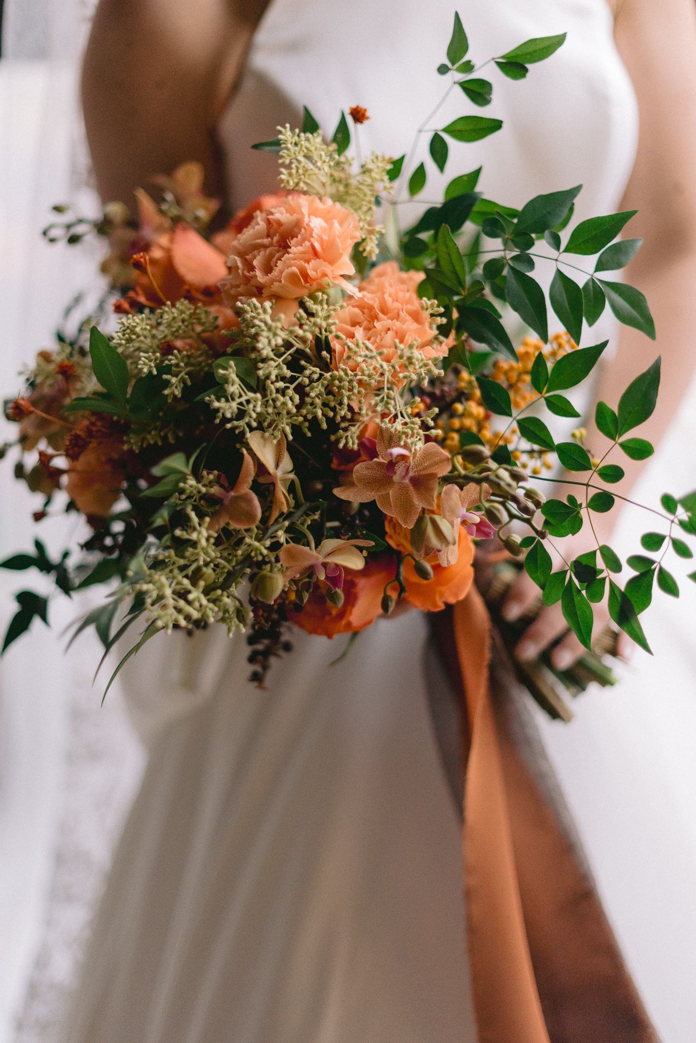 Detailed view of a lush wedding bouquet featuring coral flowers, greenery and delicate stems.