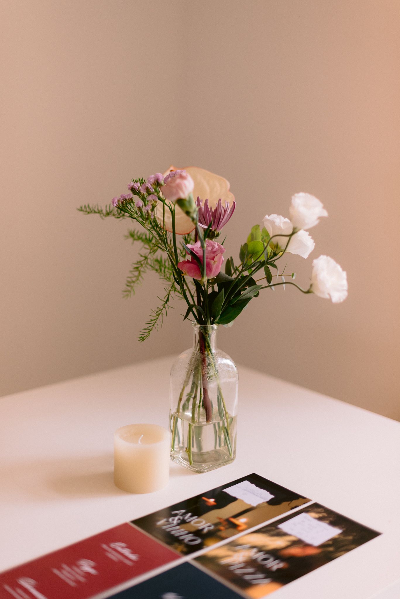 Fresh floral arrangement in vase with pink roses sits atop white table with magazines.