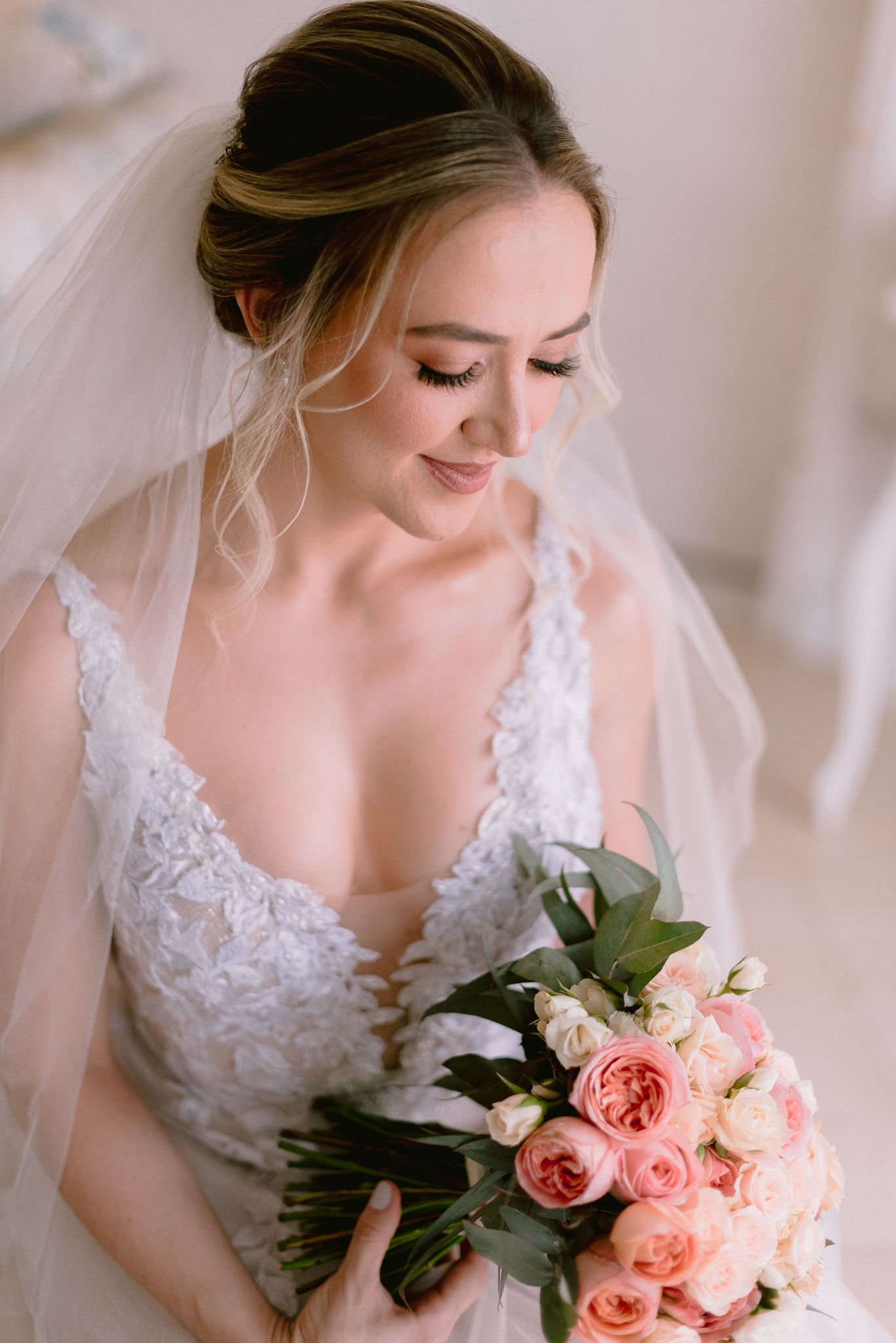 A wedding dress with intricate lace details and soft pink roses creates an elegant bridal portrait.