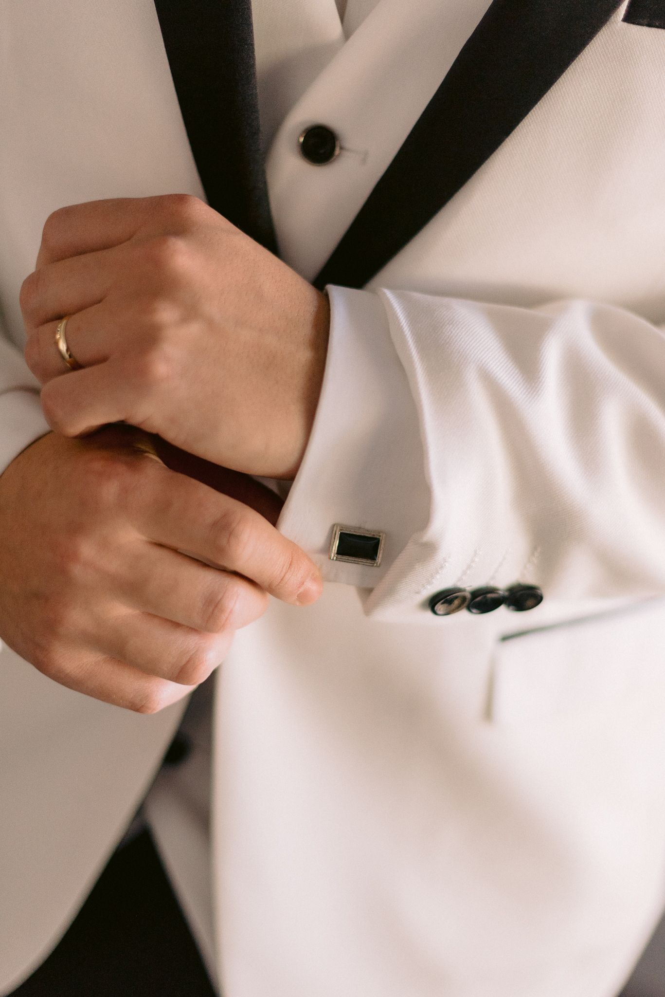 Close-up shots of hands adjusting buttons and details on a white formal tuxedo jacket.