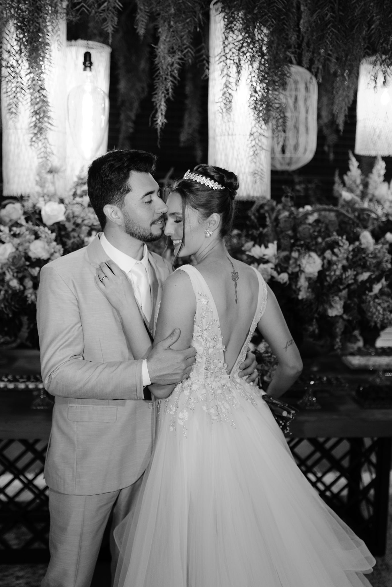 Romantic wedding couple shares tender moments in a beautifully decorated reception venue with hanging lights and greenery.