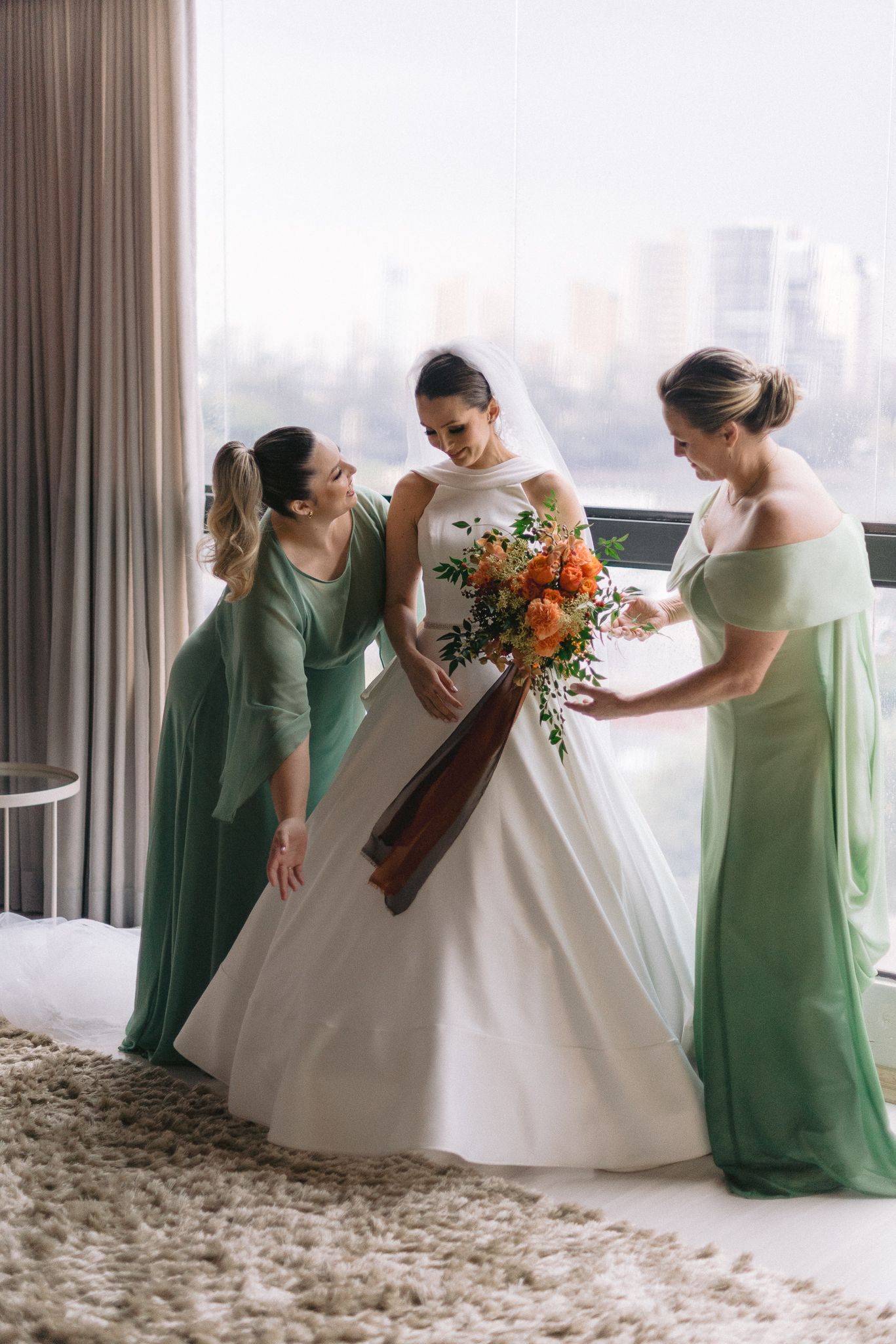 Bridesmaids in mint green dresses assist with the bride's gown preparations.