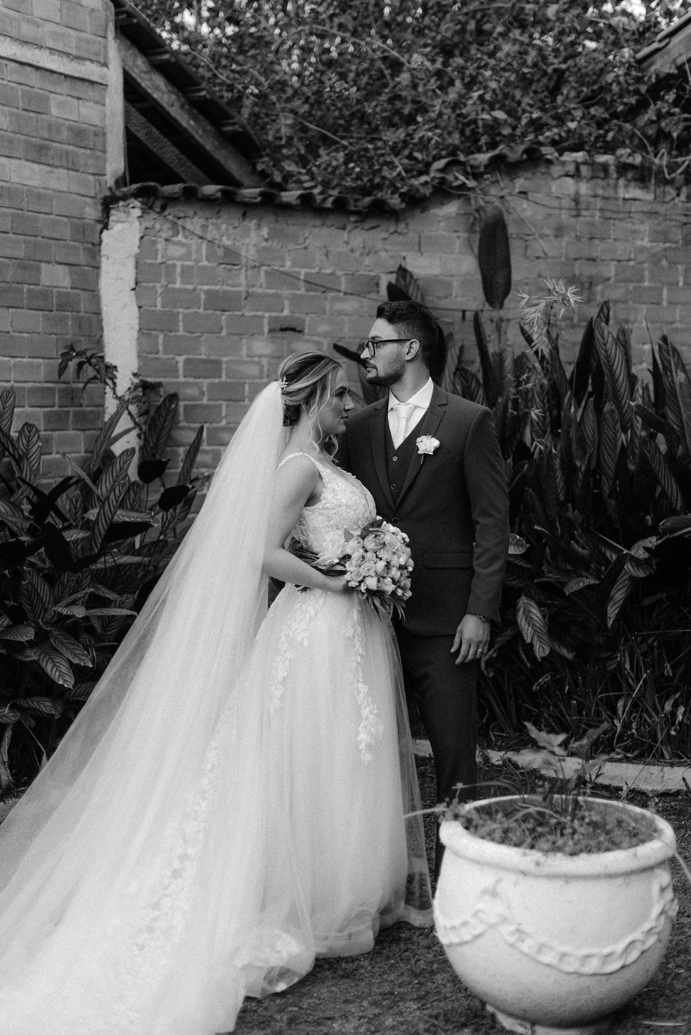 A romantic black and white wedding portrait series taken against a brick wall with garden planters.