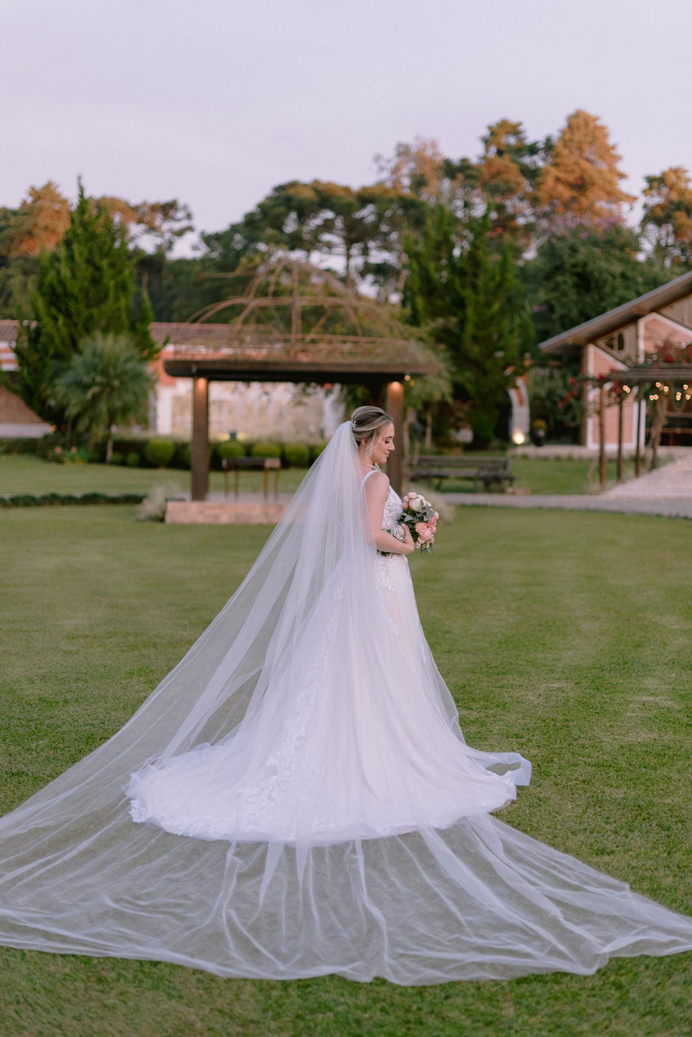 A stunning wedding dress with cathedral length veil spreads beautifully across a green lawn.
