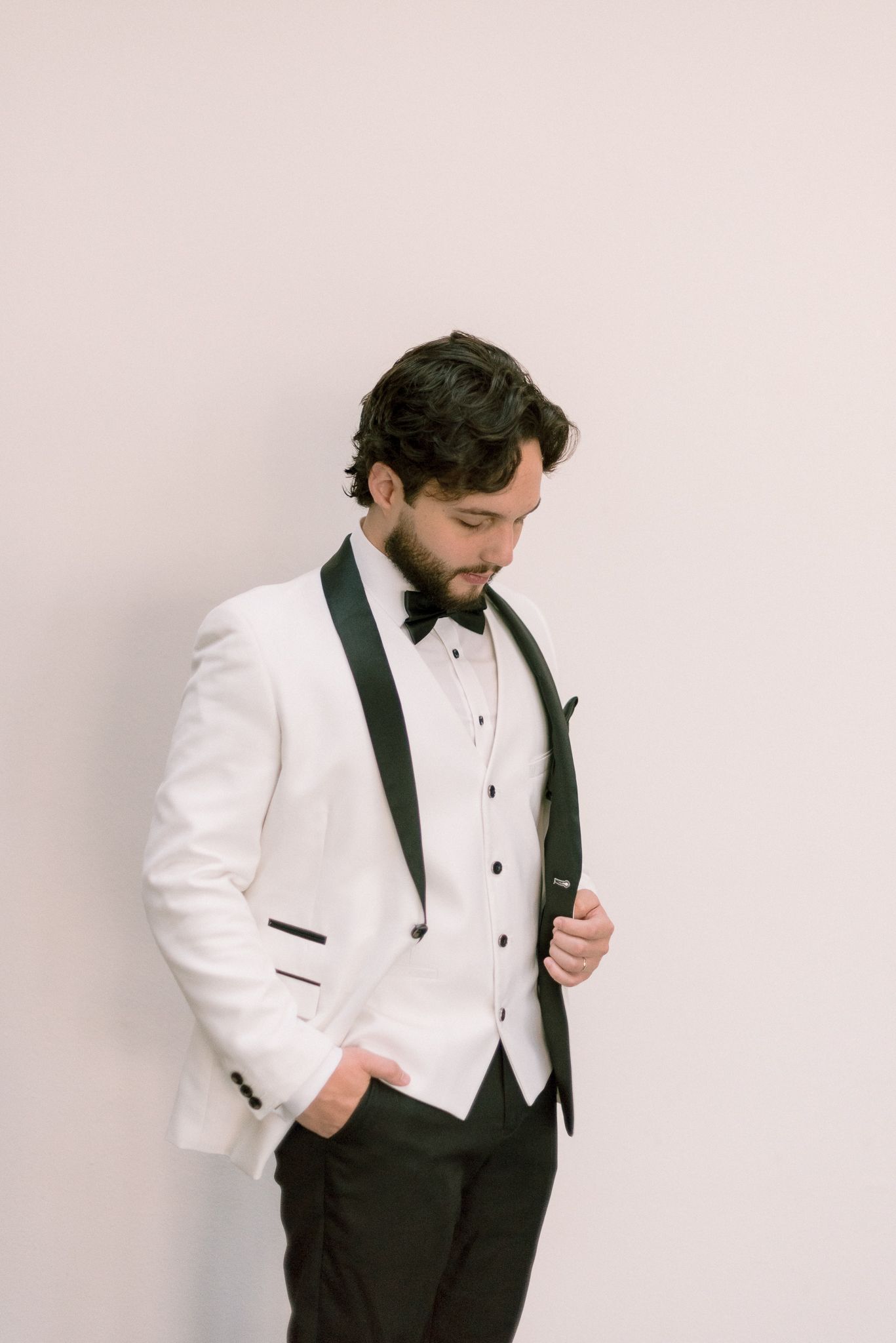 Side view of an elegant white dinner jacket with black lapels and bow tie against light background.