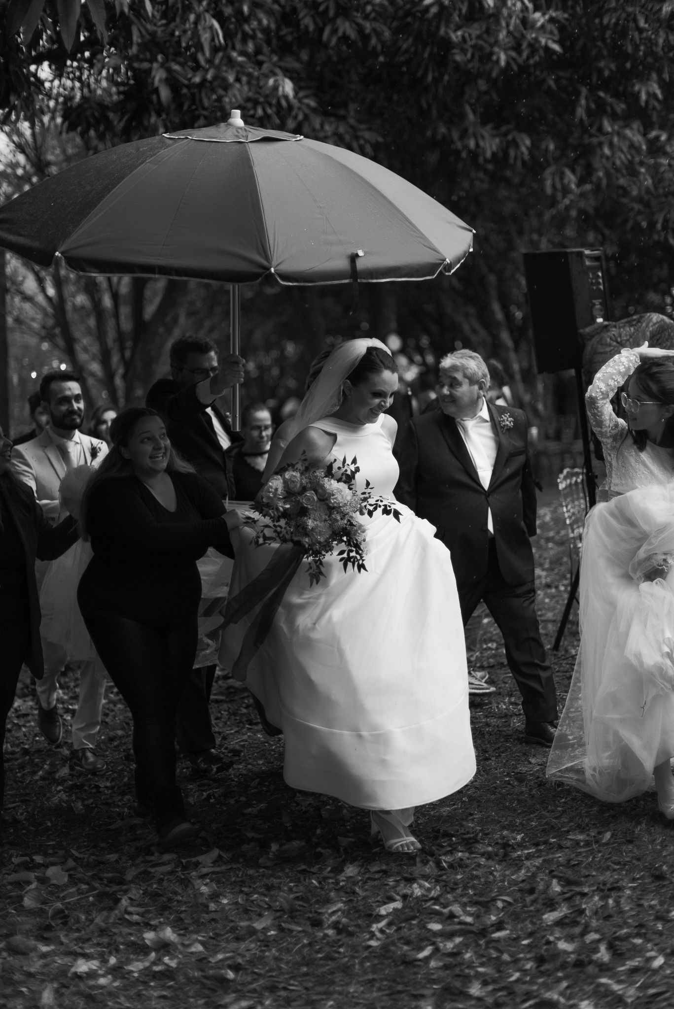 Wedding party walking through autumn leaves with black umbrellas in rain.