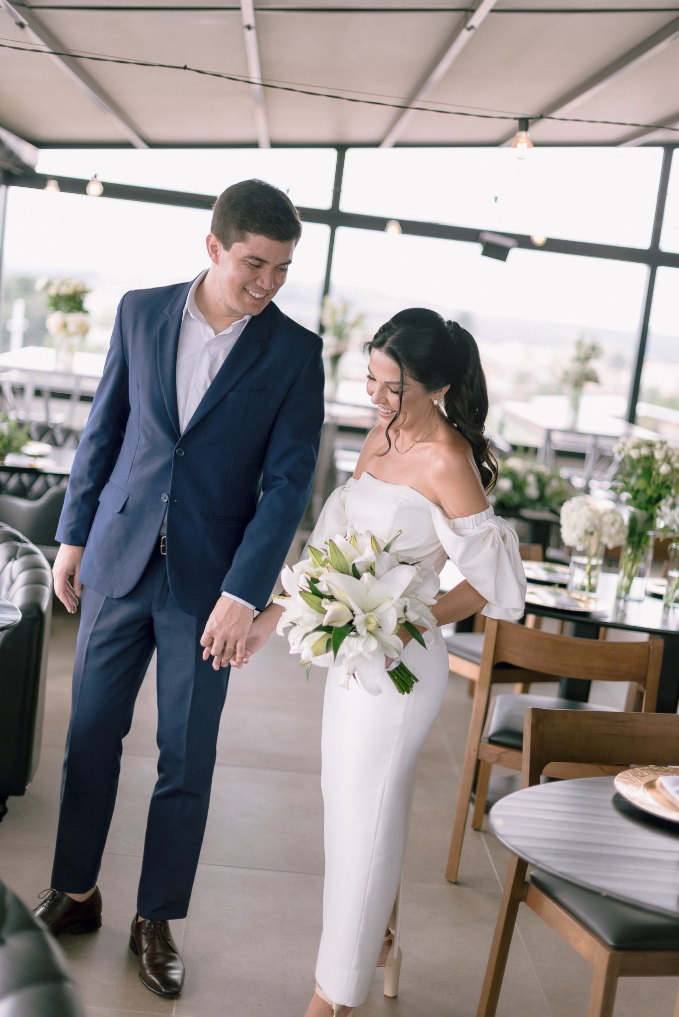 A couple featuring a navy suit and white dress pose together in an elegant indoor setting.