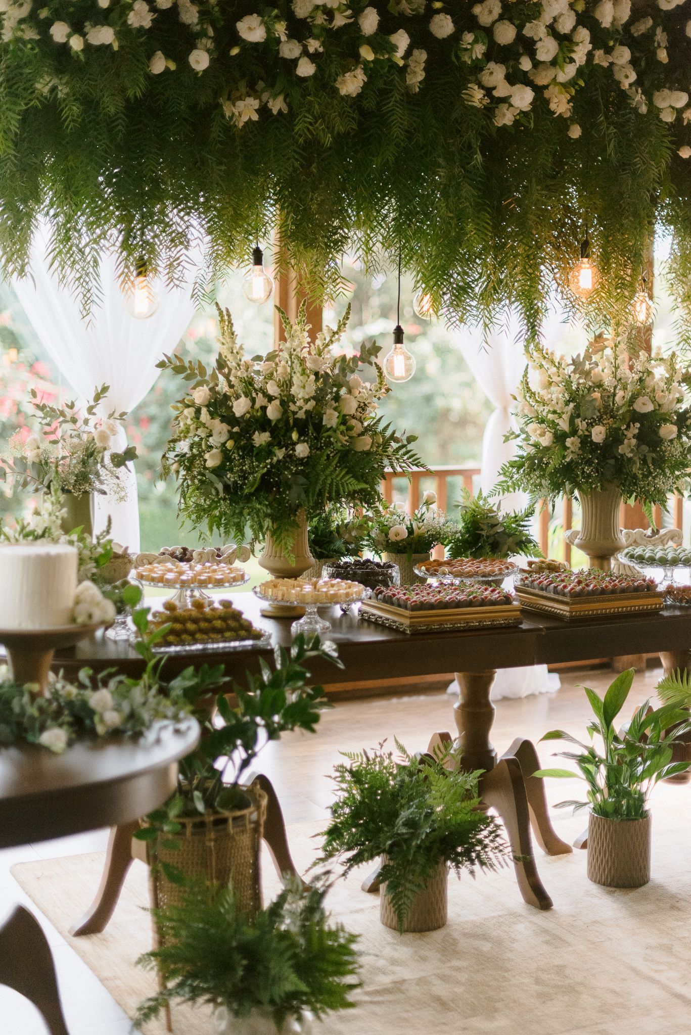 Long rustic wooden tables decorated with hanging floral arrangements and greenery create an enchanting indoor garden setting.