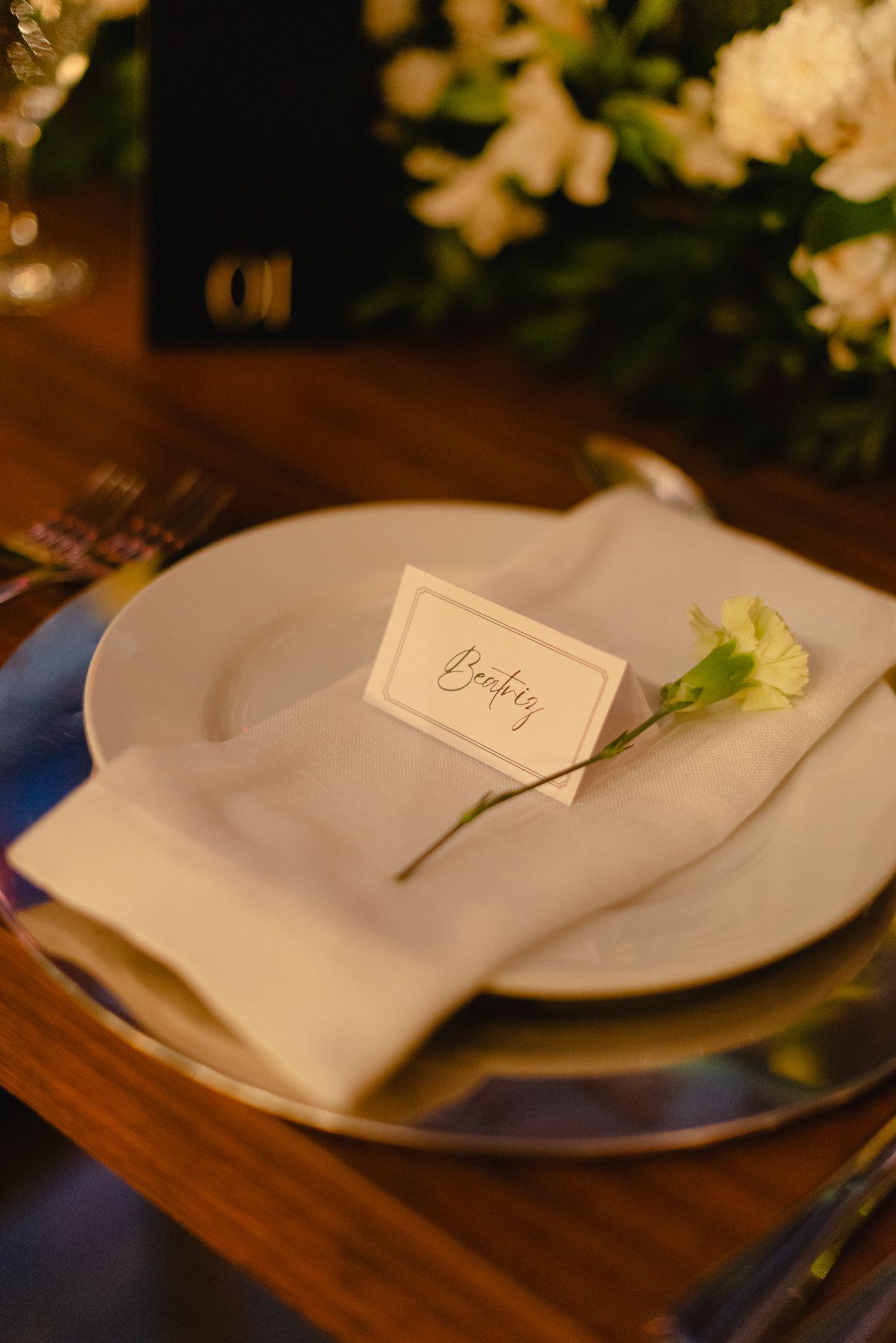 Elegant table setting with white plates, folded napkins, and place cards on a wooden surface illuminated by warm lighting.