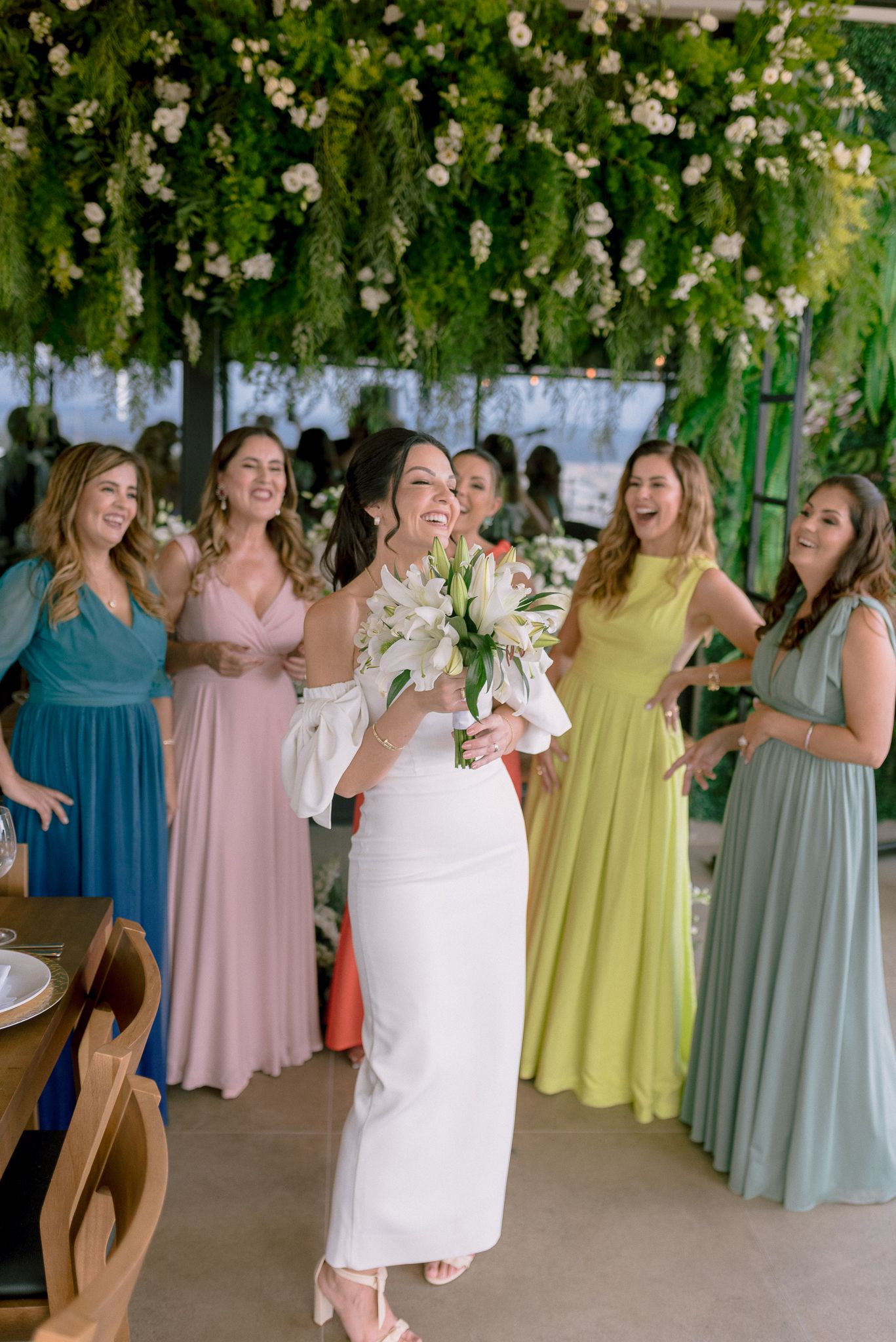 Wedding party in pastel colored bridesmaid dresses and white gown gather under floral decorations.