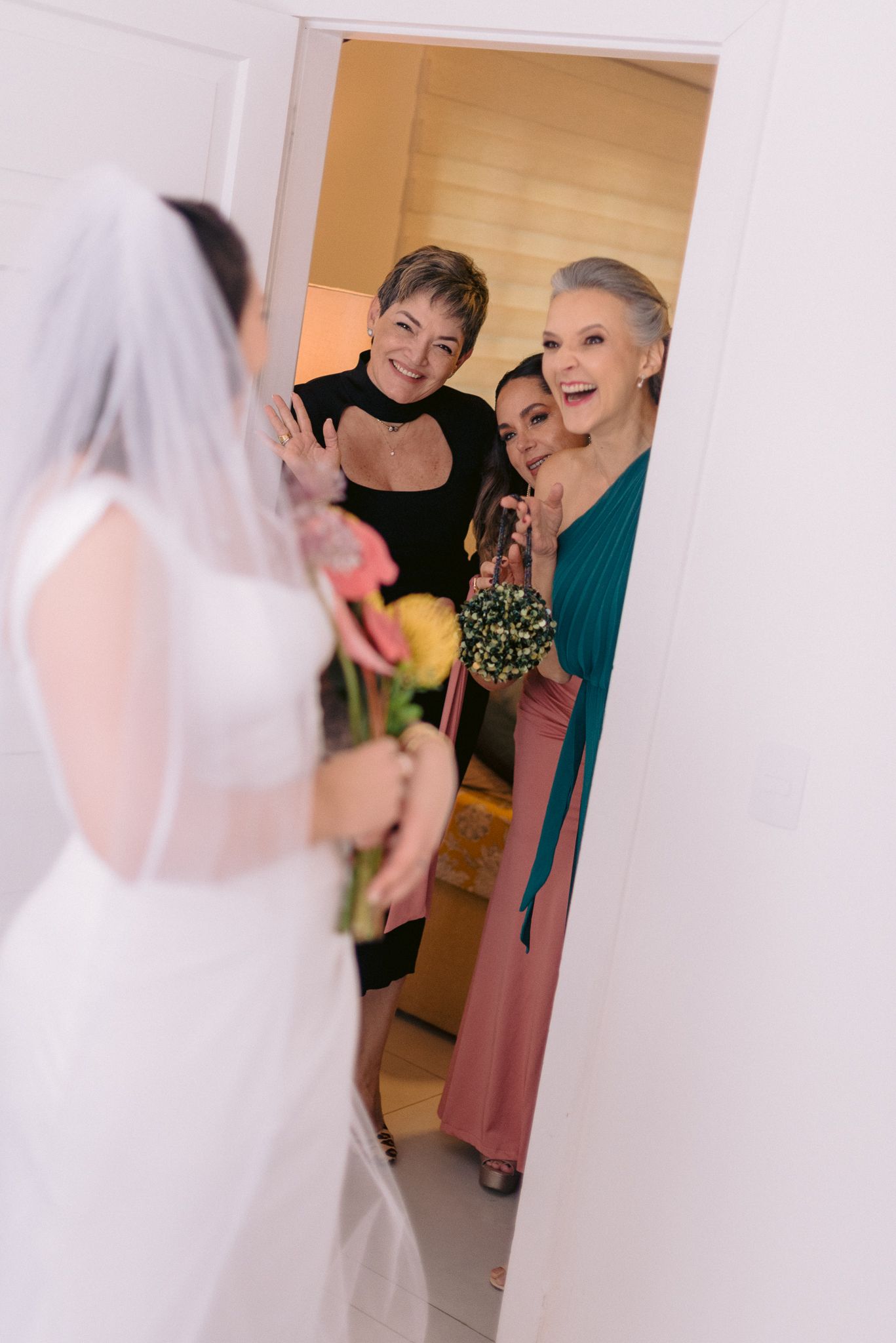 Joyful wedding reveal moment captured through doorway with bride in white veil.